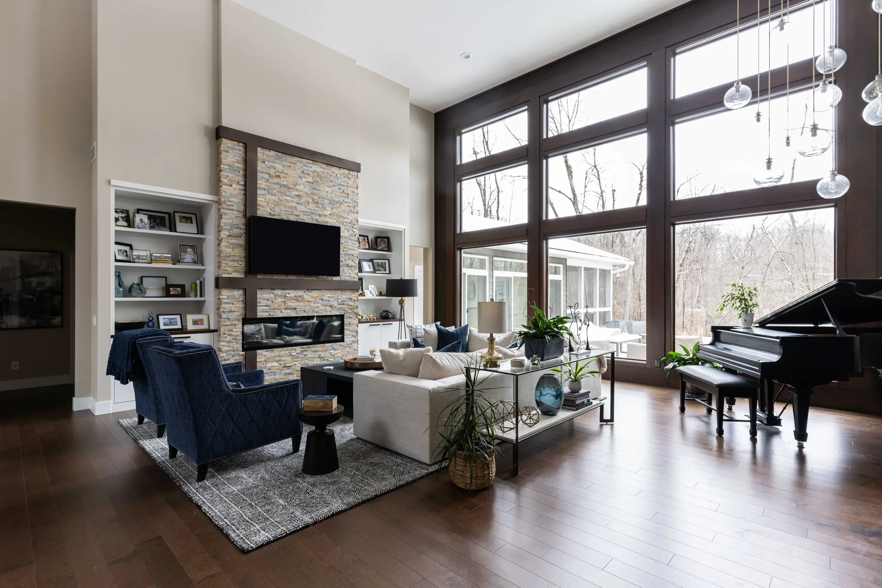 Modern living room with stone fireplace, custom cabinetry, hardwood floors, and large windows
