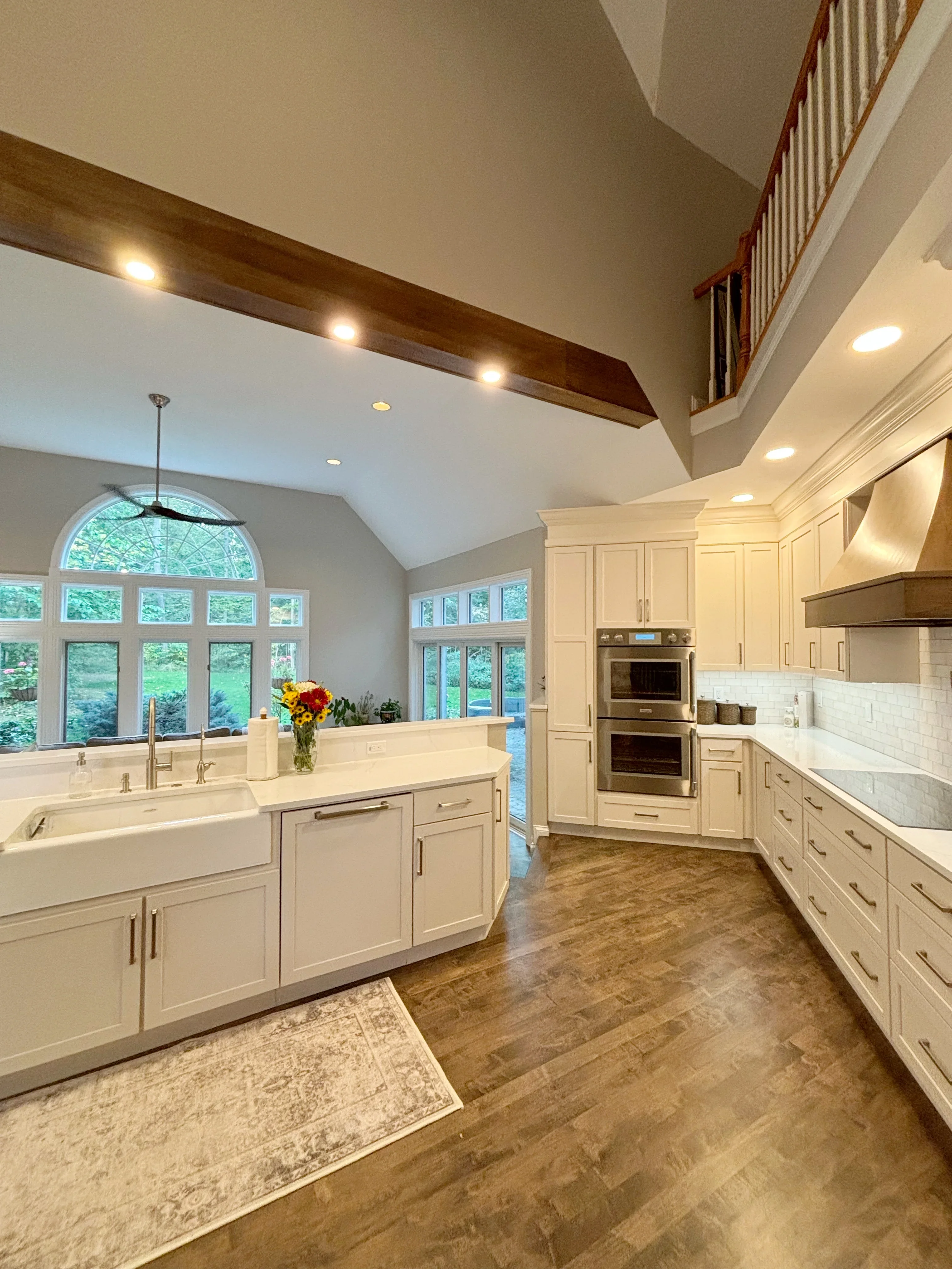 Cream cabinetry kitchen with island, double ovens, wood beams, and large windows