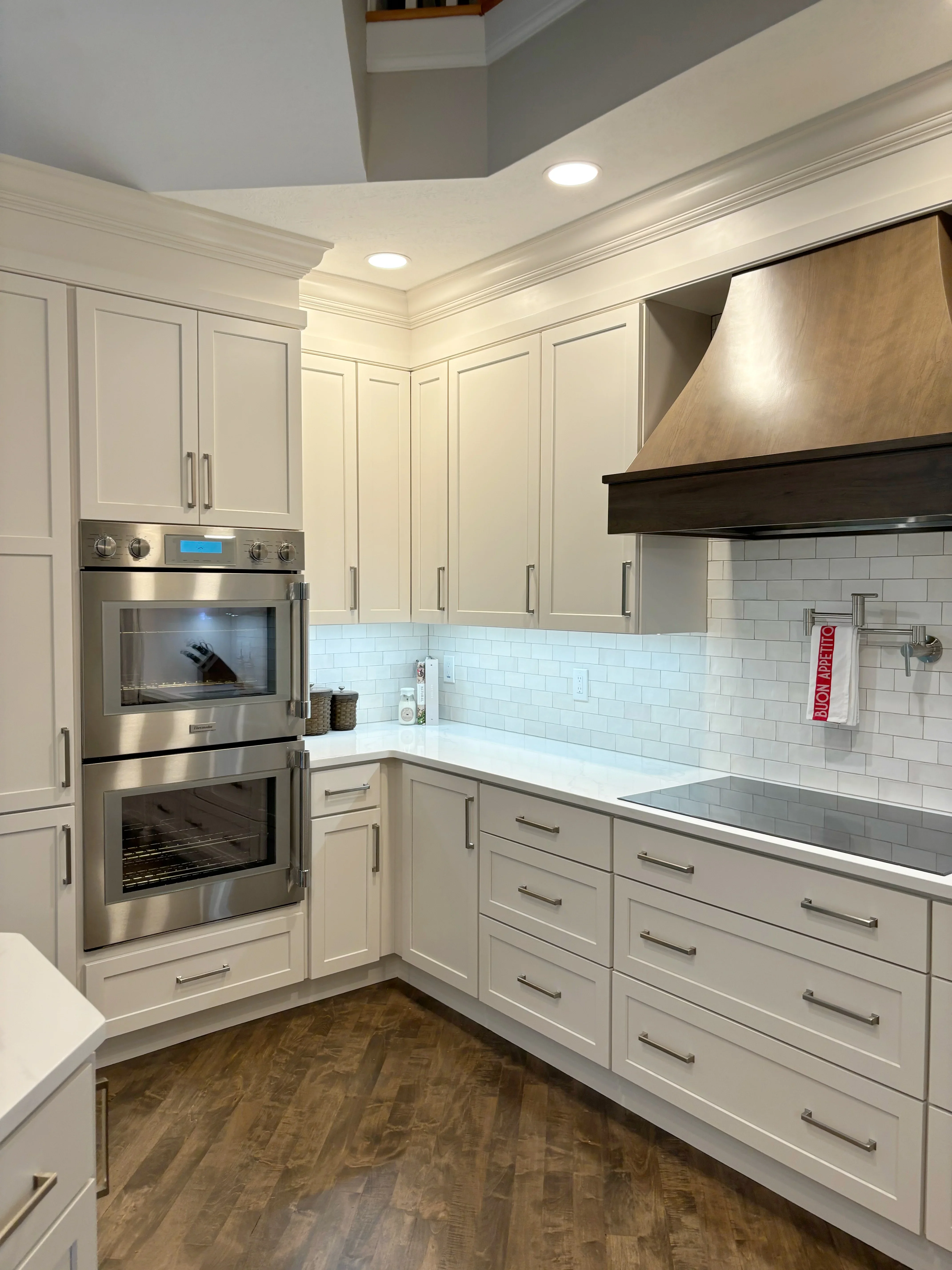 White kitchen with dual stainless steel ovens, subway tile backsplash, custom cabinetry, and wood range hood