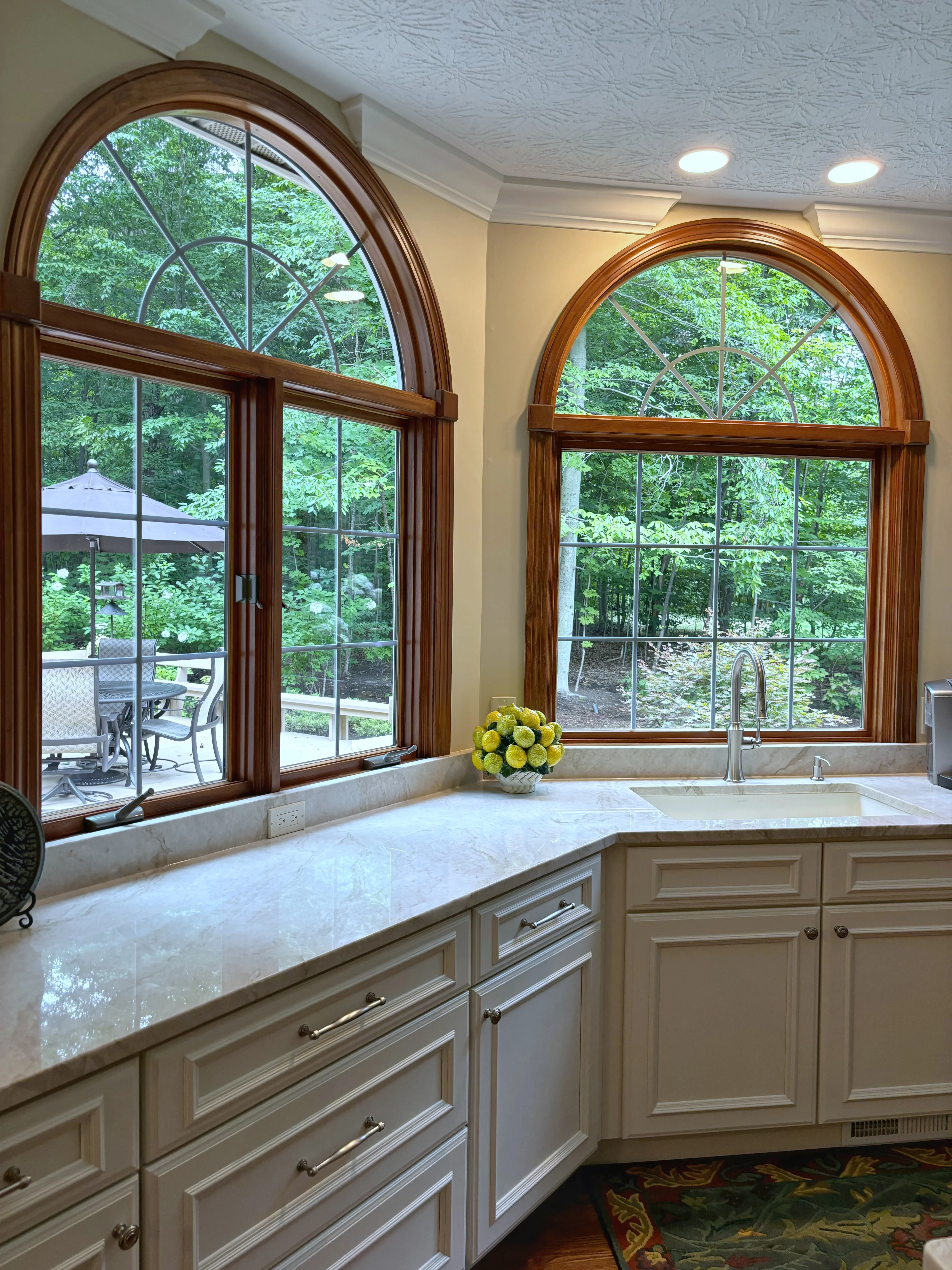 Kitchen with cream cabinetry, marble counters, and two arched wood windows with grid panes