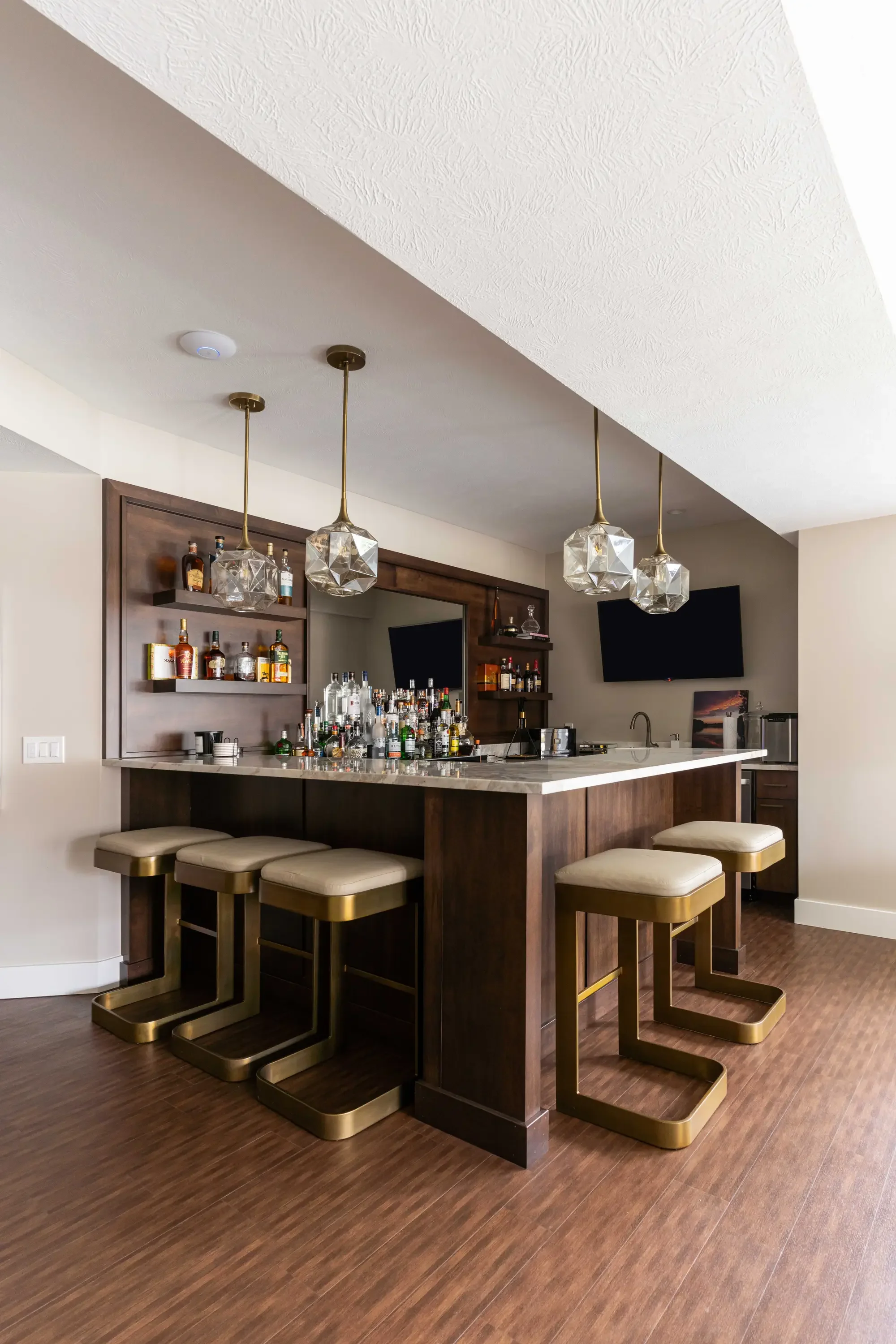 Dark walnut bar cabinetry with quartz countertop, brass bar stools, and geometric glass pendant lights