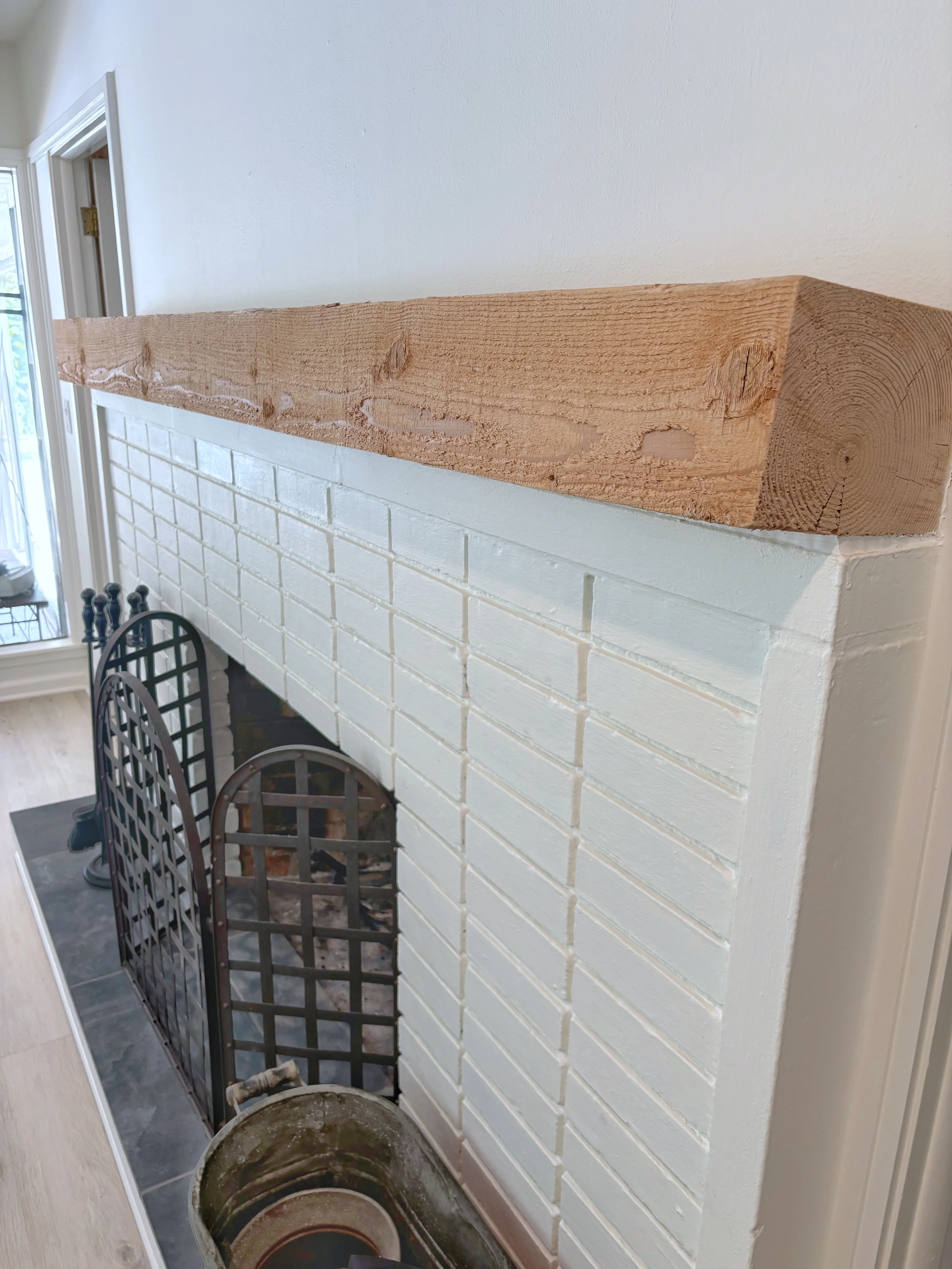 White subway tile fireplace surround with reclaimed wood mantel and iron screen