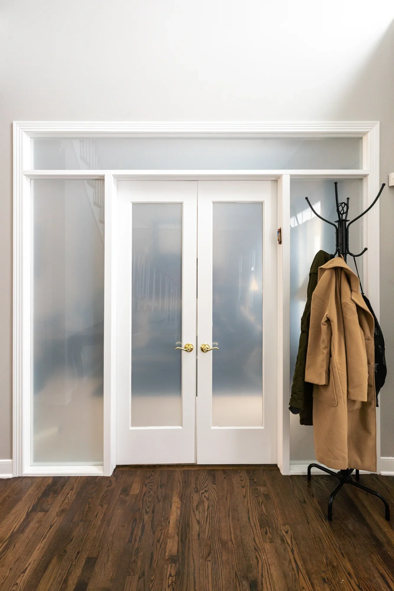White French door closet with frosted glass panels, brass hardware, and built-in shelving above hardwood floor