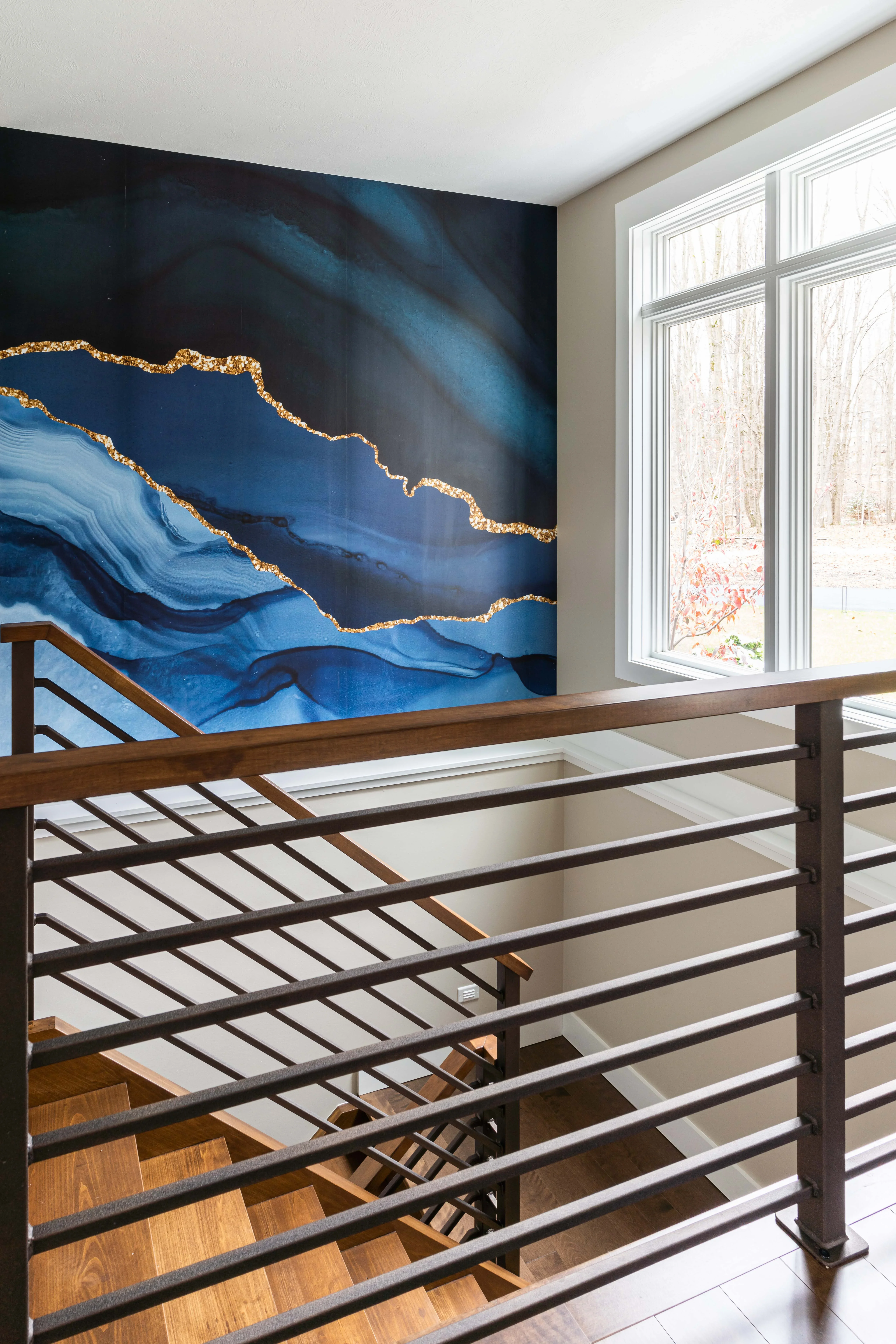 Modern staircase with dark metal railing, wood steps, and blue-gold abstract feature wall