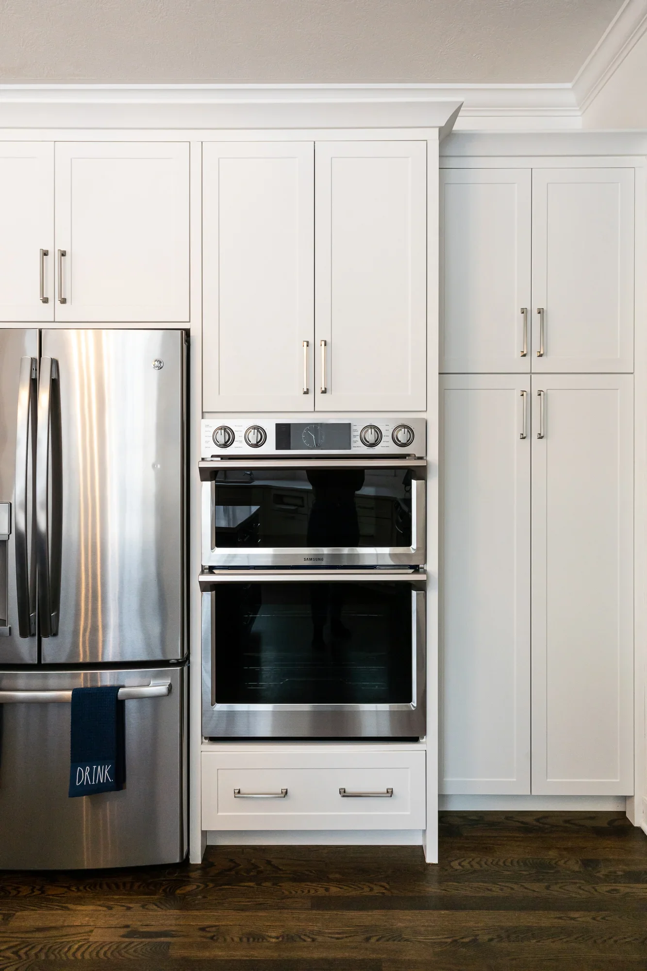 White kitchen cabinetry with stainless steel double wall oven and refrigerator, brushed nickel hardware