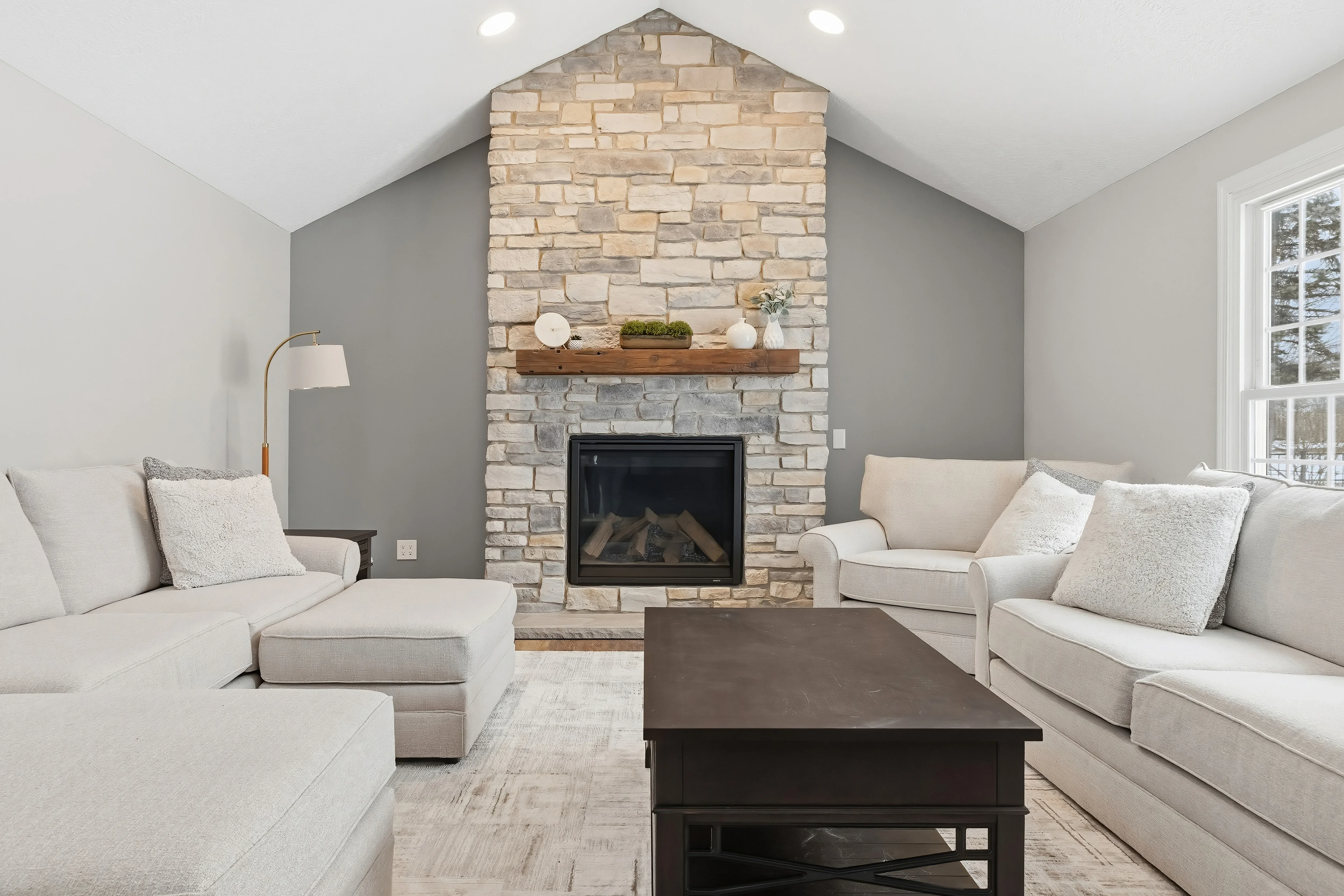 Stacked stone fireplace with wood mantel, vaulted ceiling, and recessed lighting in renovated living room