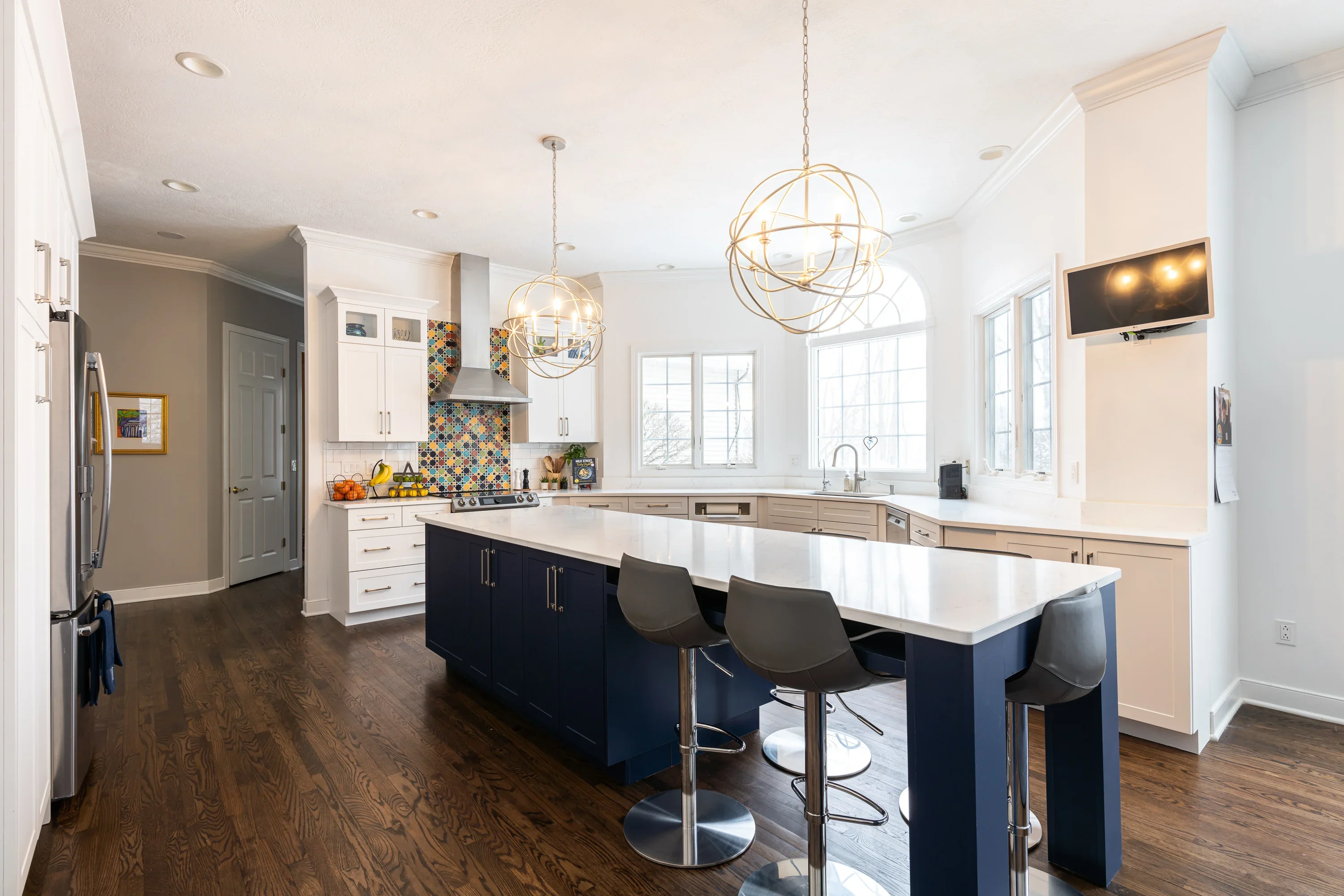Modern kitchen with white and navy cabinetry, white quartz counters, geometric tile backsplash, and brass pendant lights