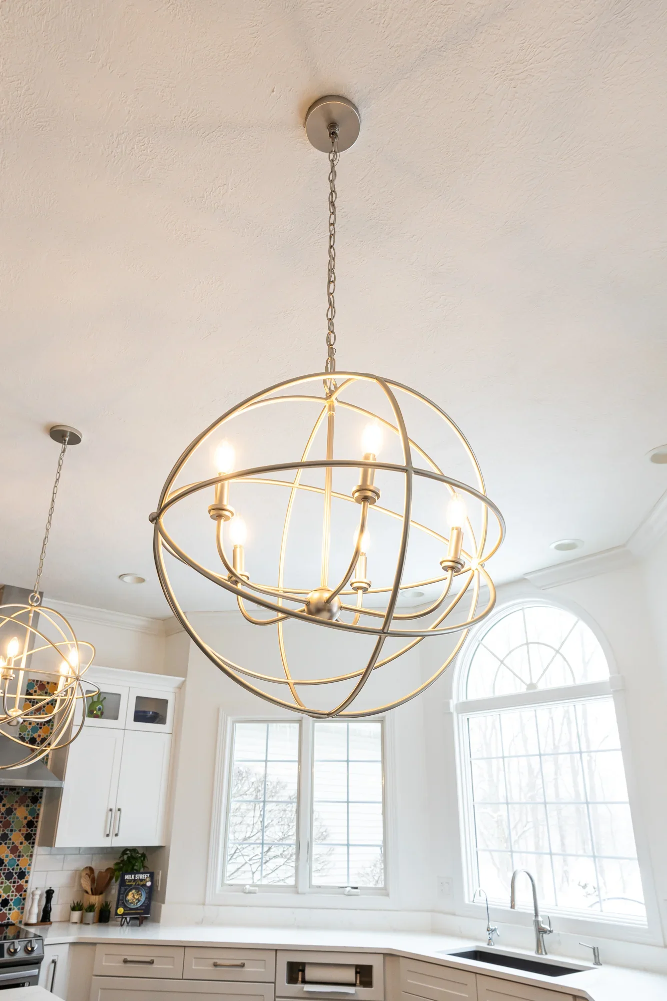 Brass orbital pendant light in modern kitchen with white cabinetry and quartz counters