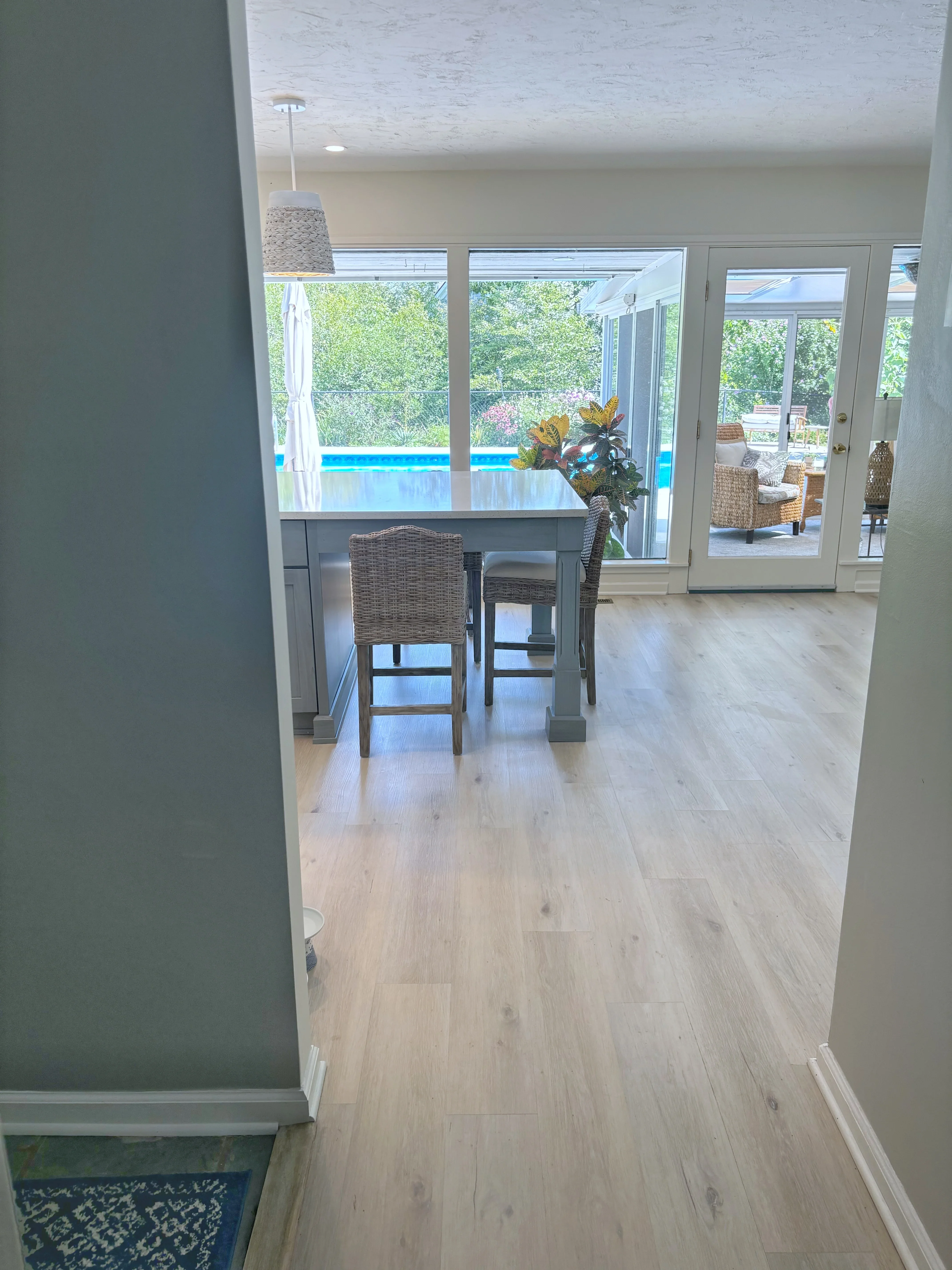 Light oak flooring, glass doors, bar counter with rattan stools, pool view