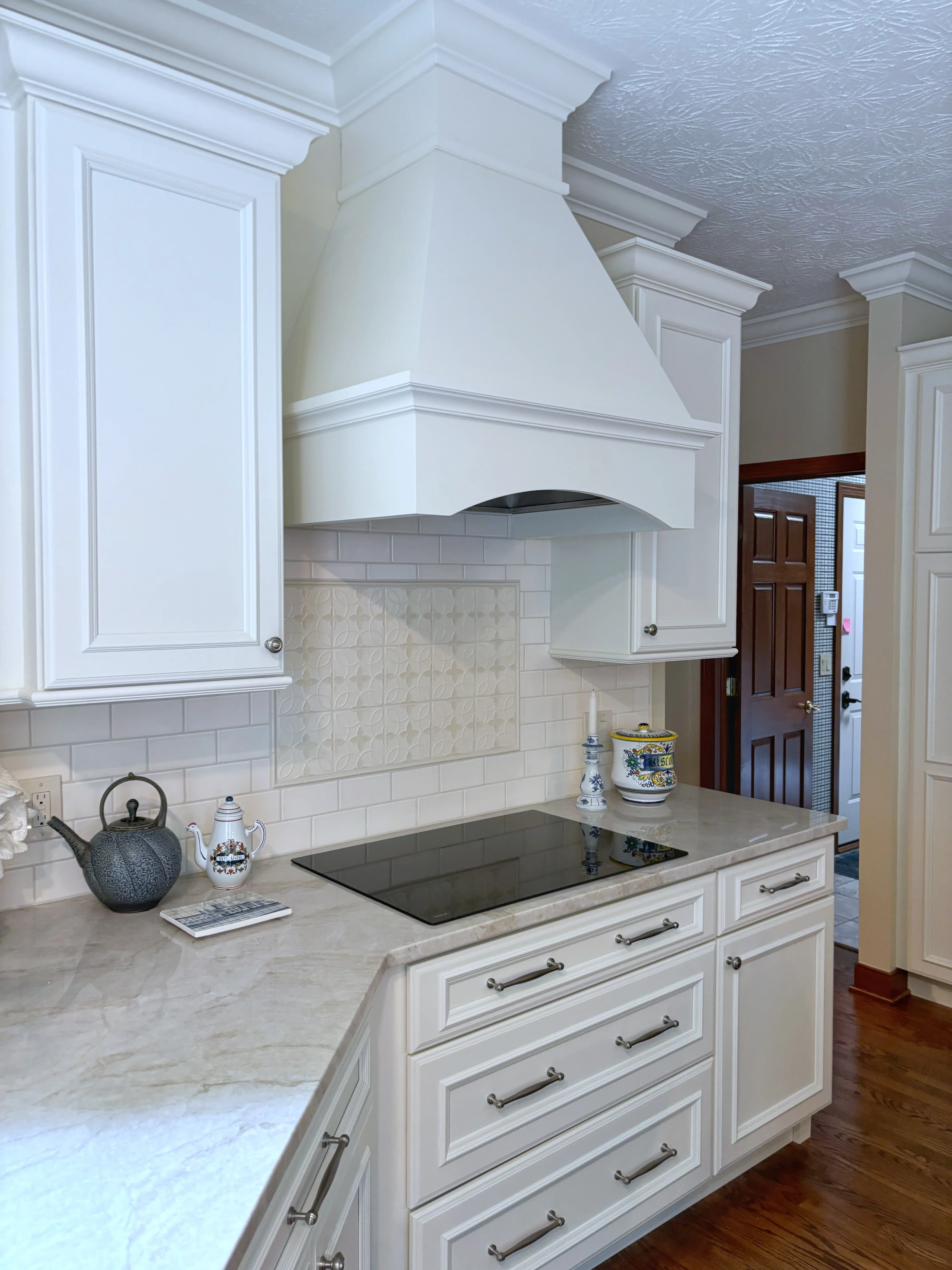White kitchen with shaker cabinets, marble counters, subway tile backsplash, and custom range hood