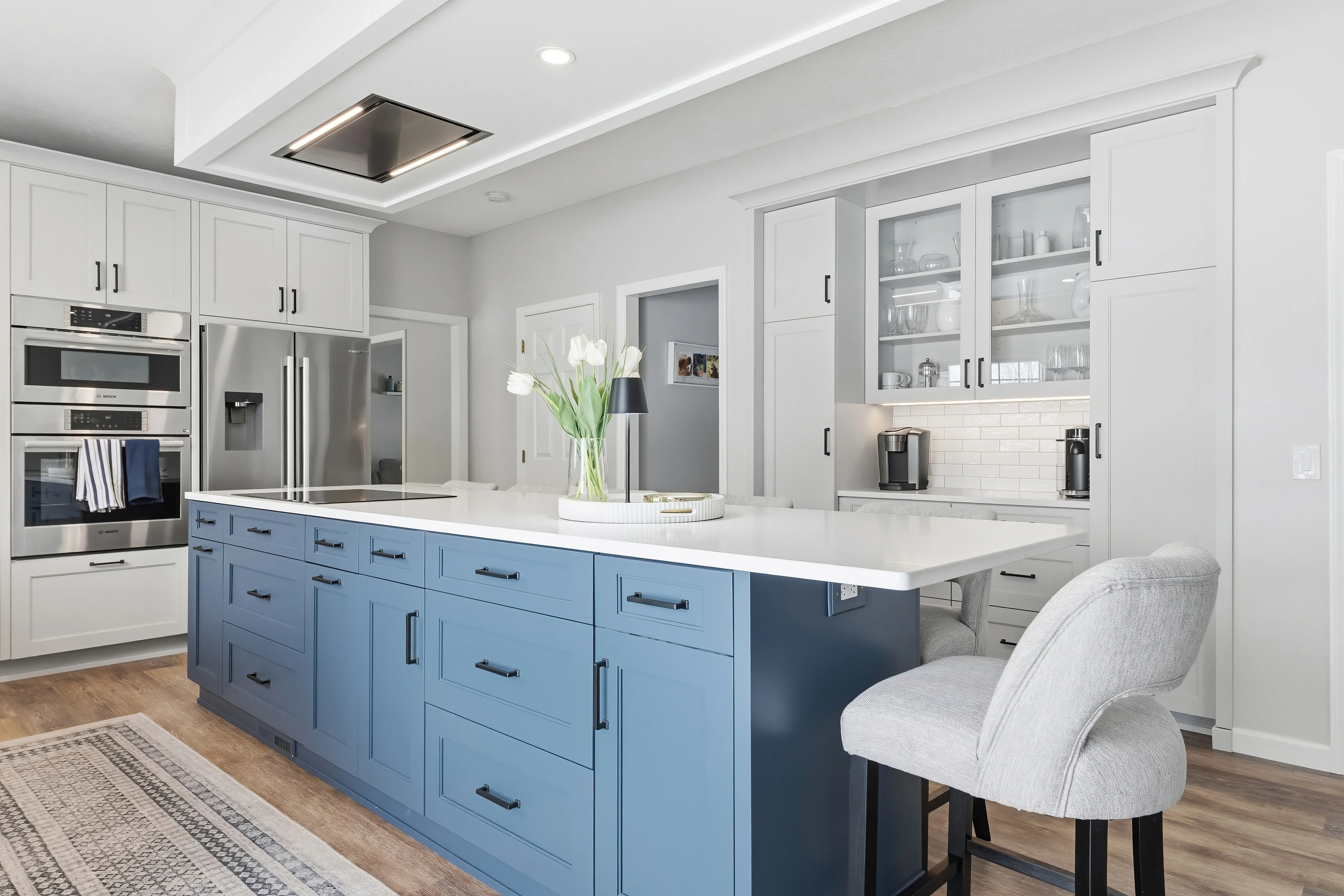 Modern kitchen with white and blue cabinetry, quartz counters, stainless steel appliances, and coffered ceiling