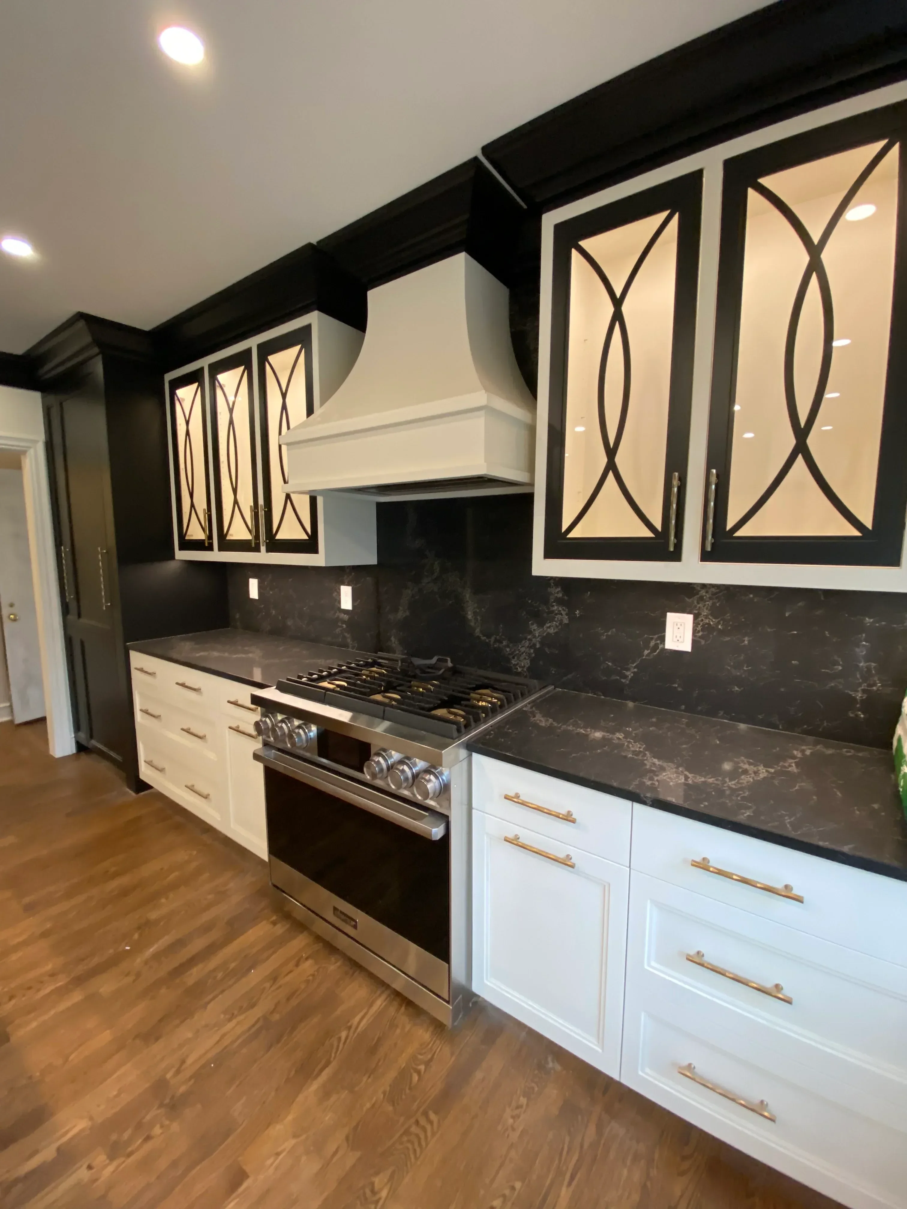 Custom white cabinetry with geometric glass doors, black marble backsplash, brass handles, and stainless steel appliances