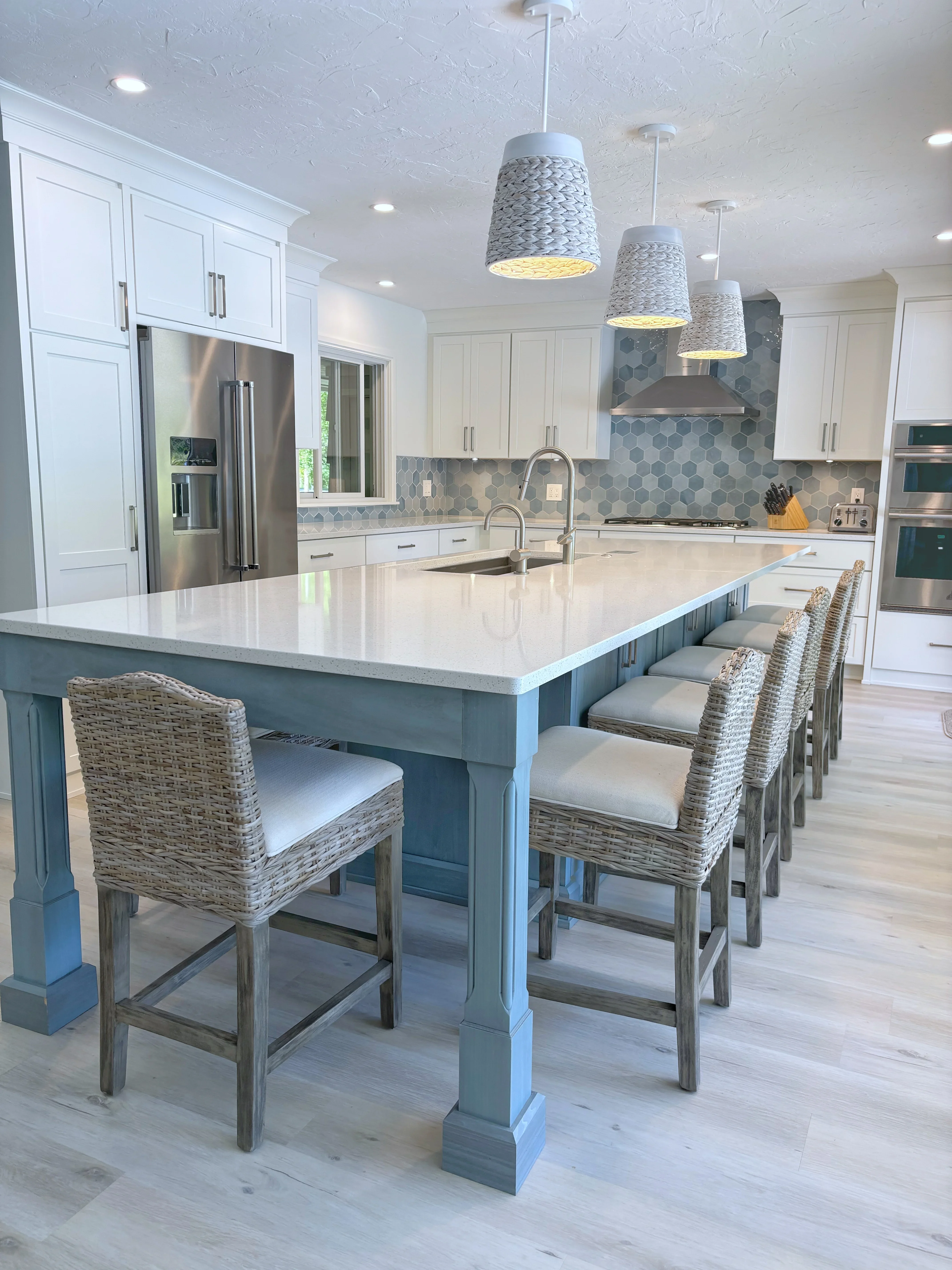 Modern kitchen with white cabinets, quartz island, teal base, rattan bar stools, and hexagonal tile backsplash