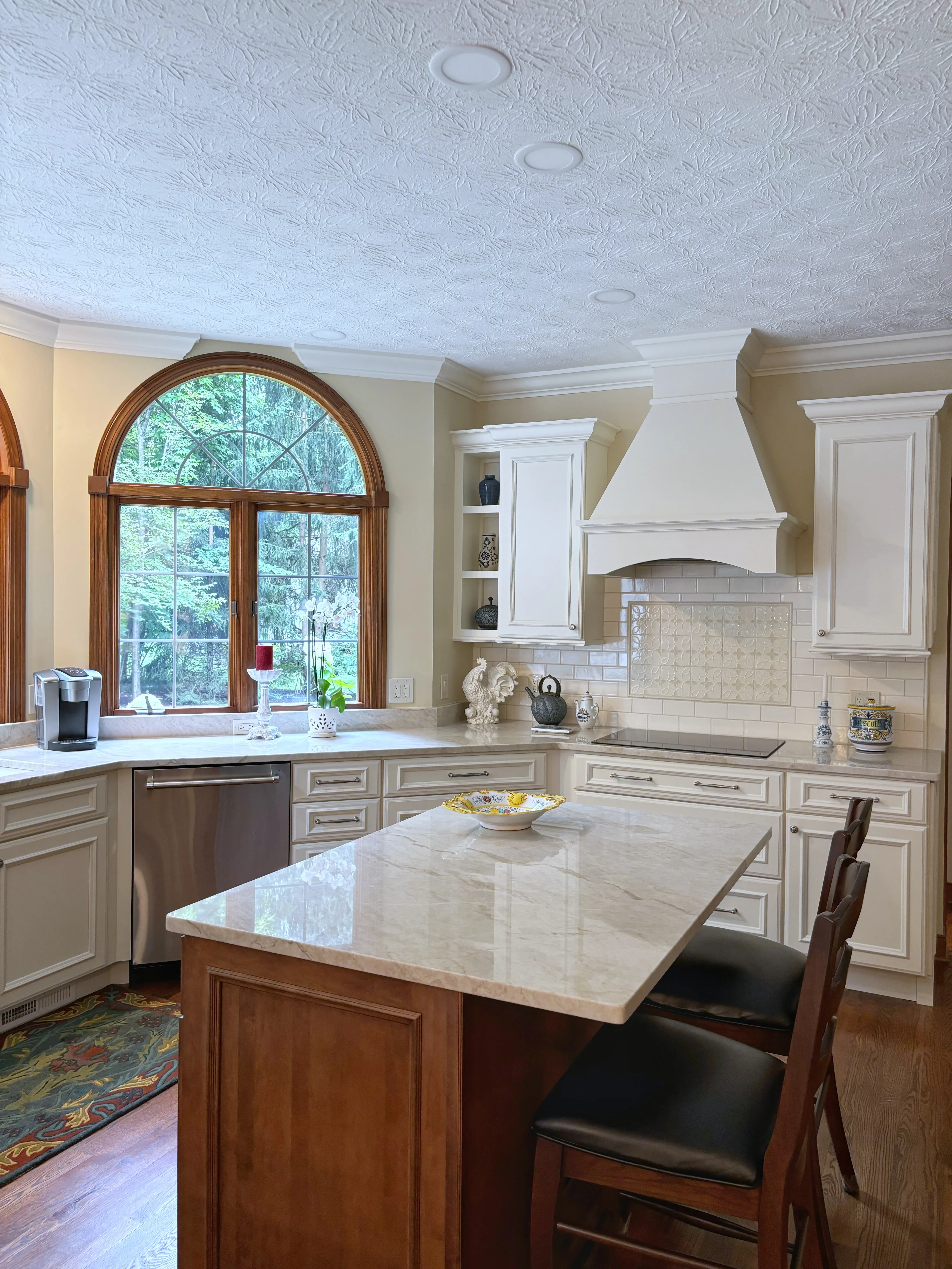 Kitchen with cream cabinetry, marble island, subway tile backsplash, and arched window
