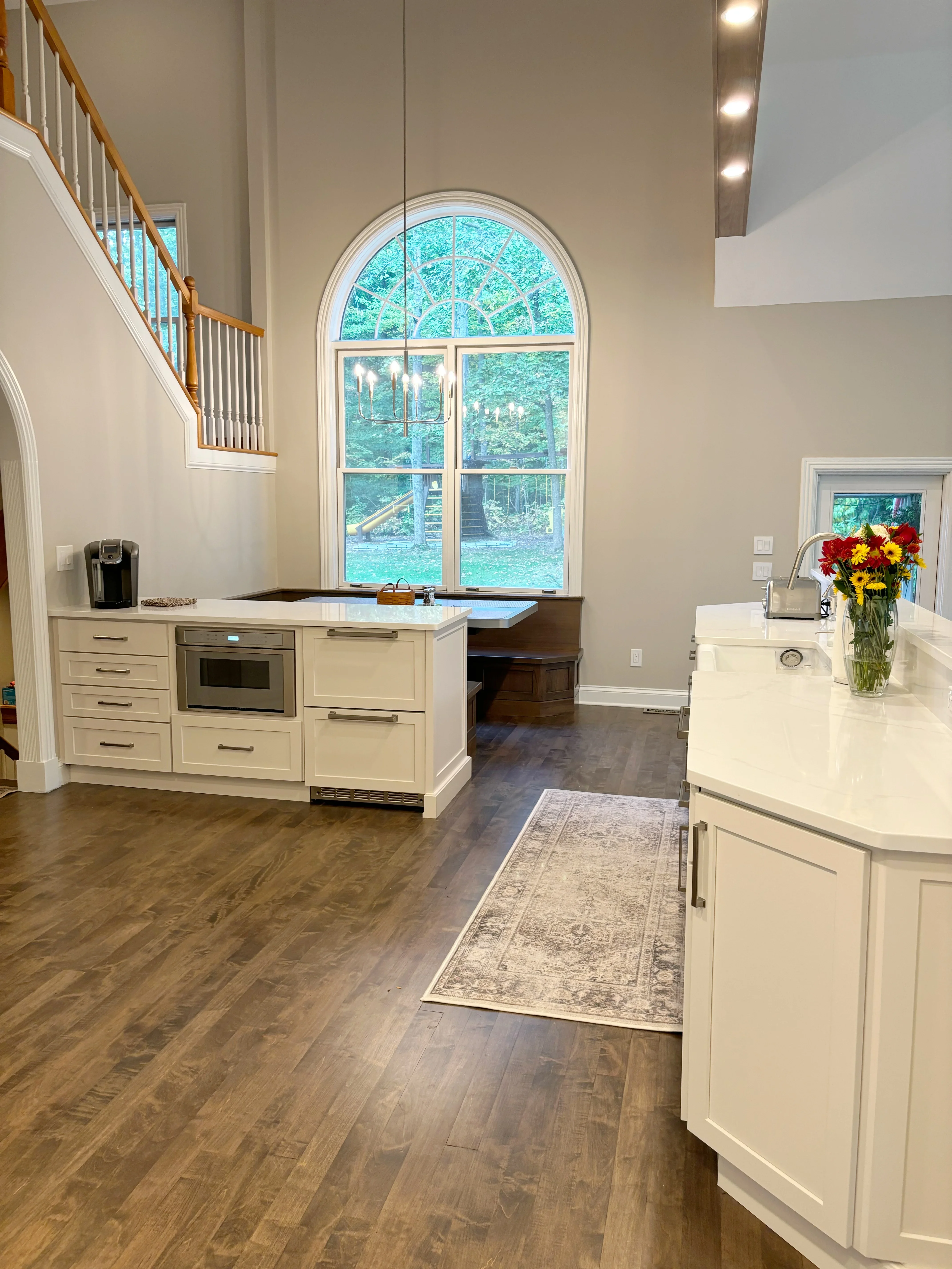 Cream cabinetry, quartz counters, wood flooring, and arched window in contemporary kitchen