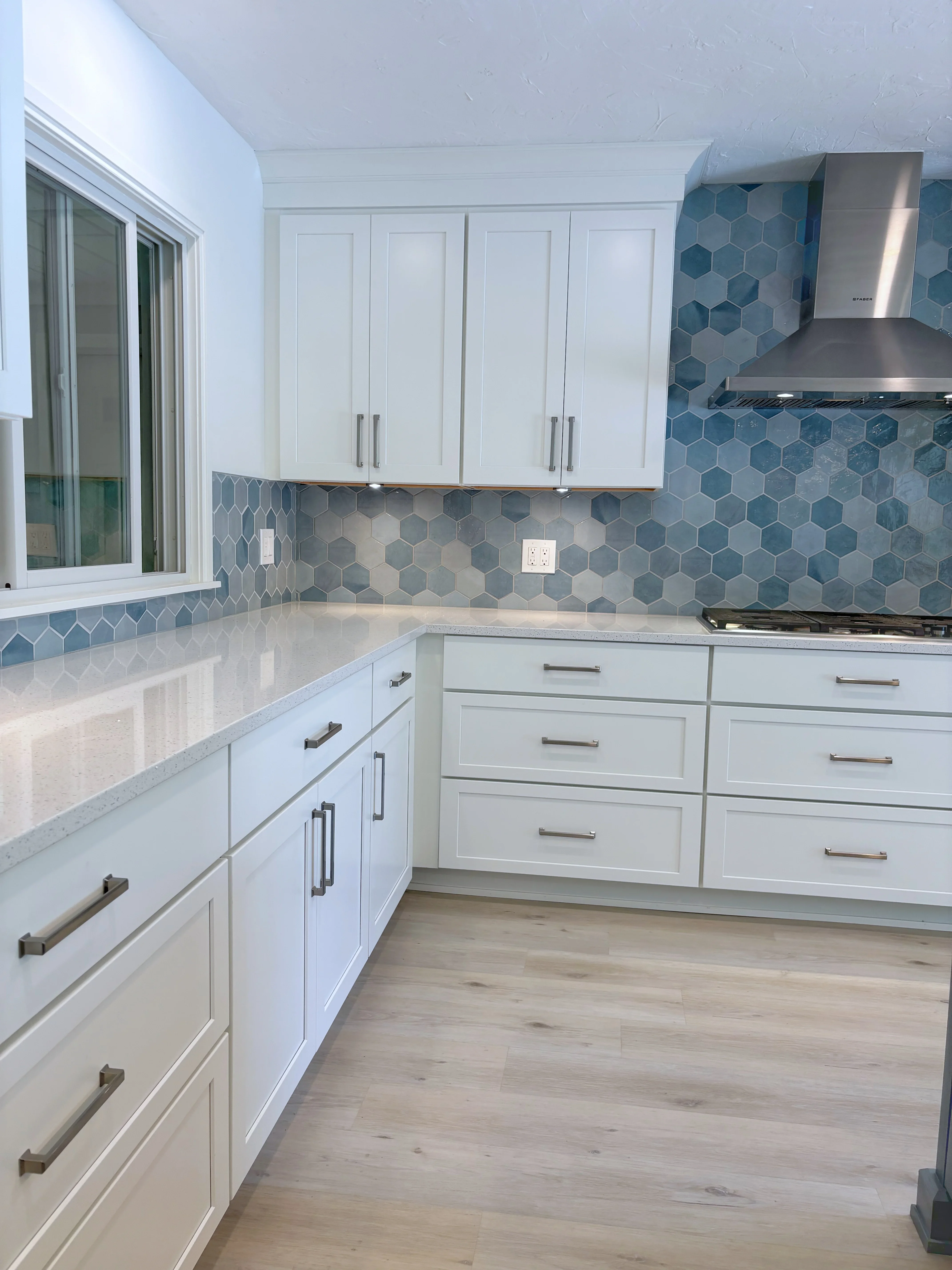 White kitchen cabinets with blue hexagon tile backsplash, quartz counters, and stainless steel range hood