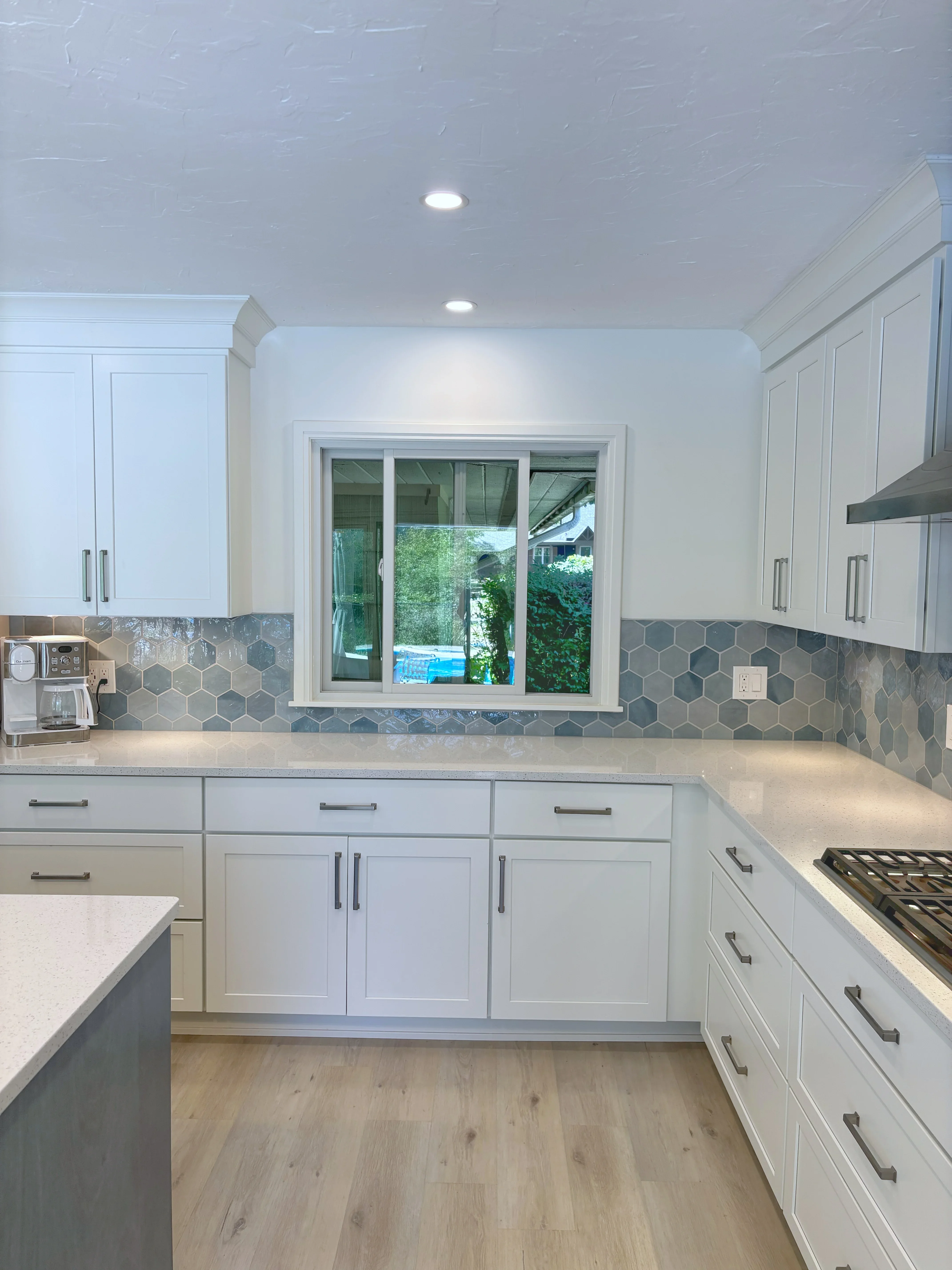 White kitchen with hexagon tile backsplash, quartz counters, and sliding glass window