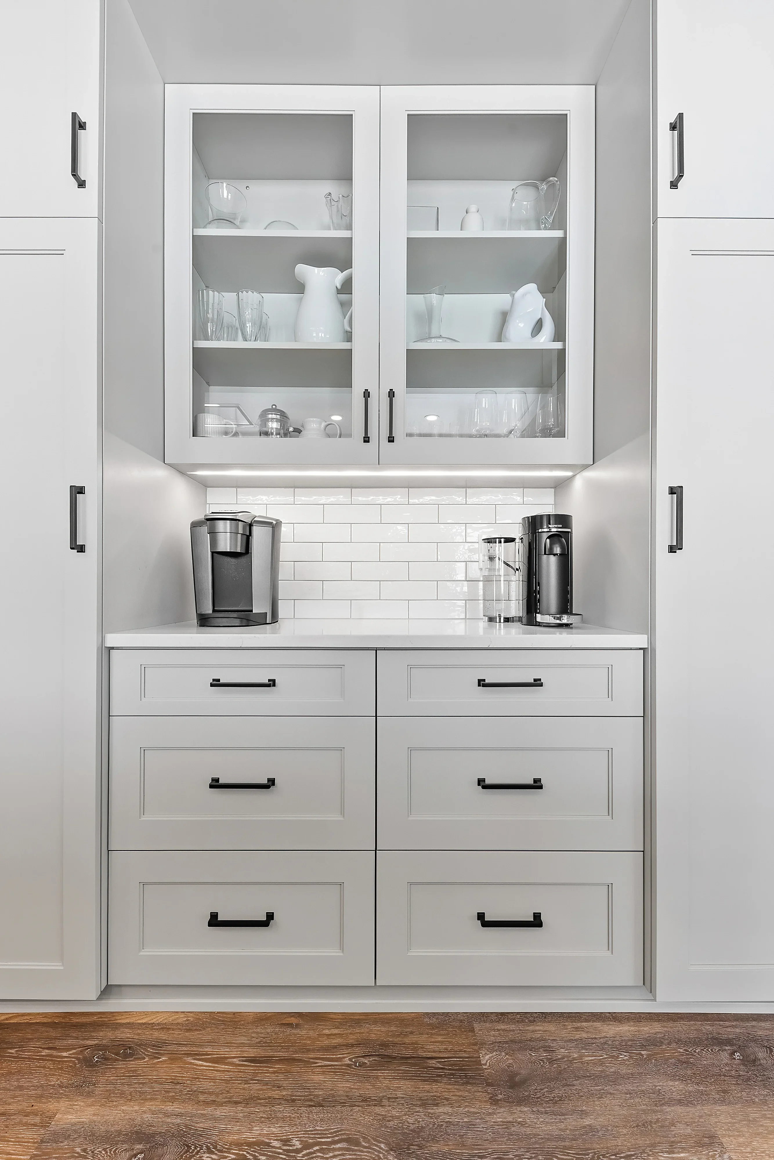 White shaker cabinetry with glass doors, subway tile backsplash, and quartz countertop