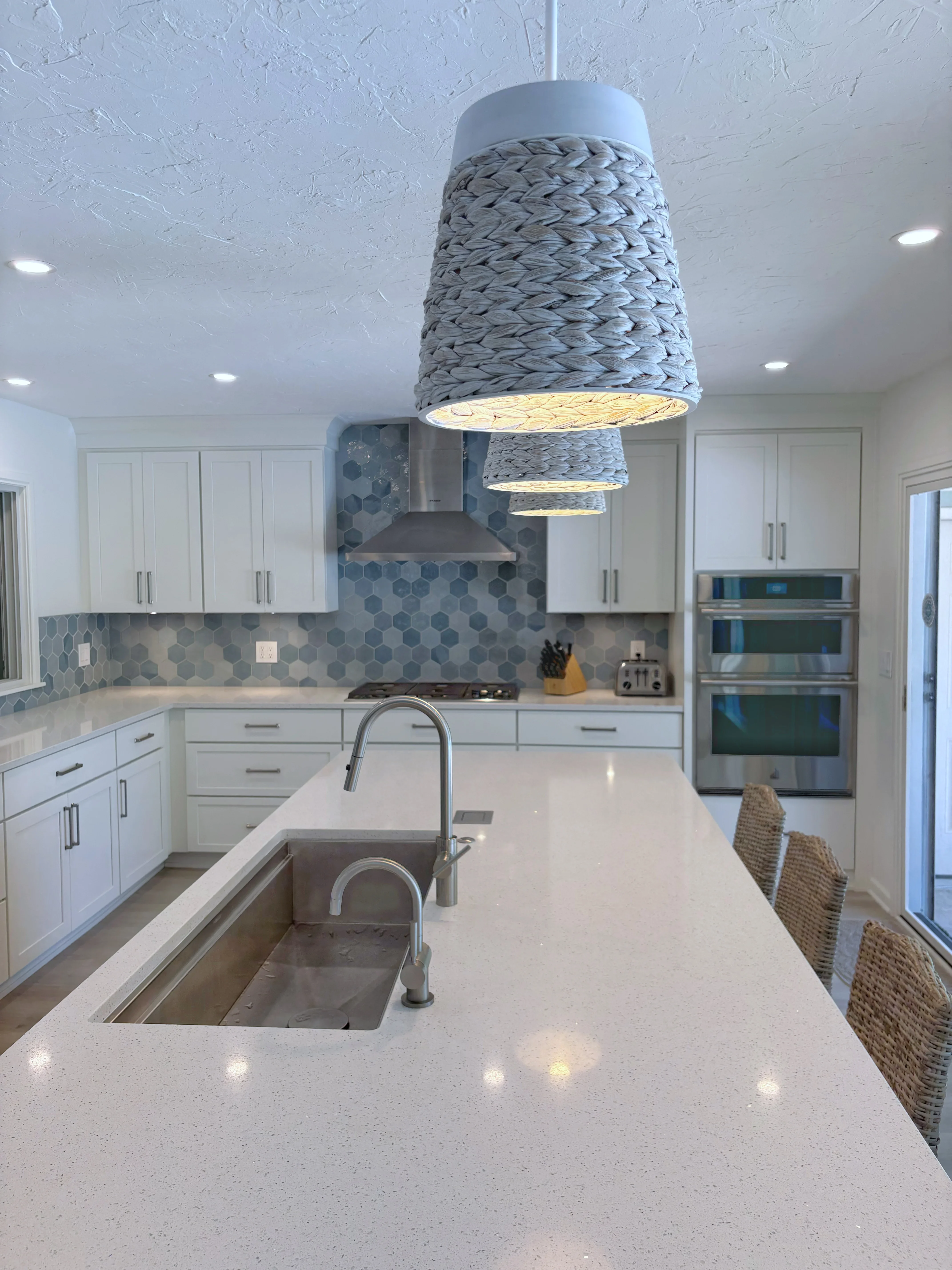 White kitchen with quartz counters, hexagon tile backsplash, and woven pendant lights