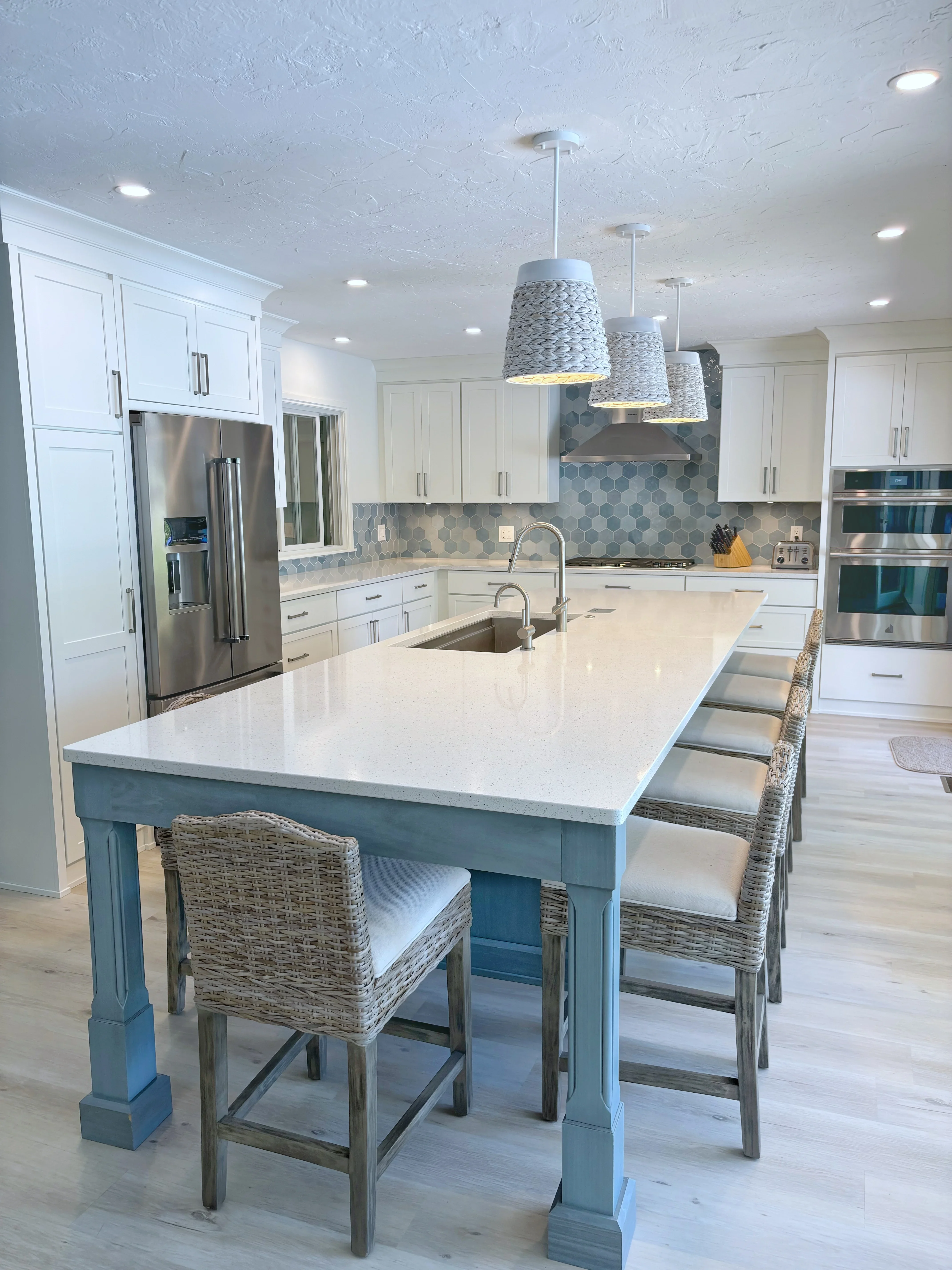 White kitchen cabinets, teal island, quartz counters, hexagonal tile backsplash, stainless steel appliances