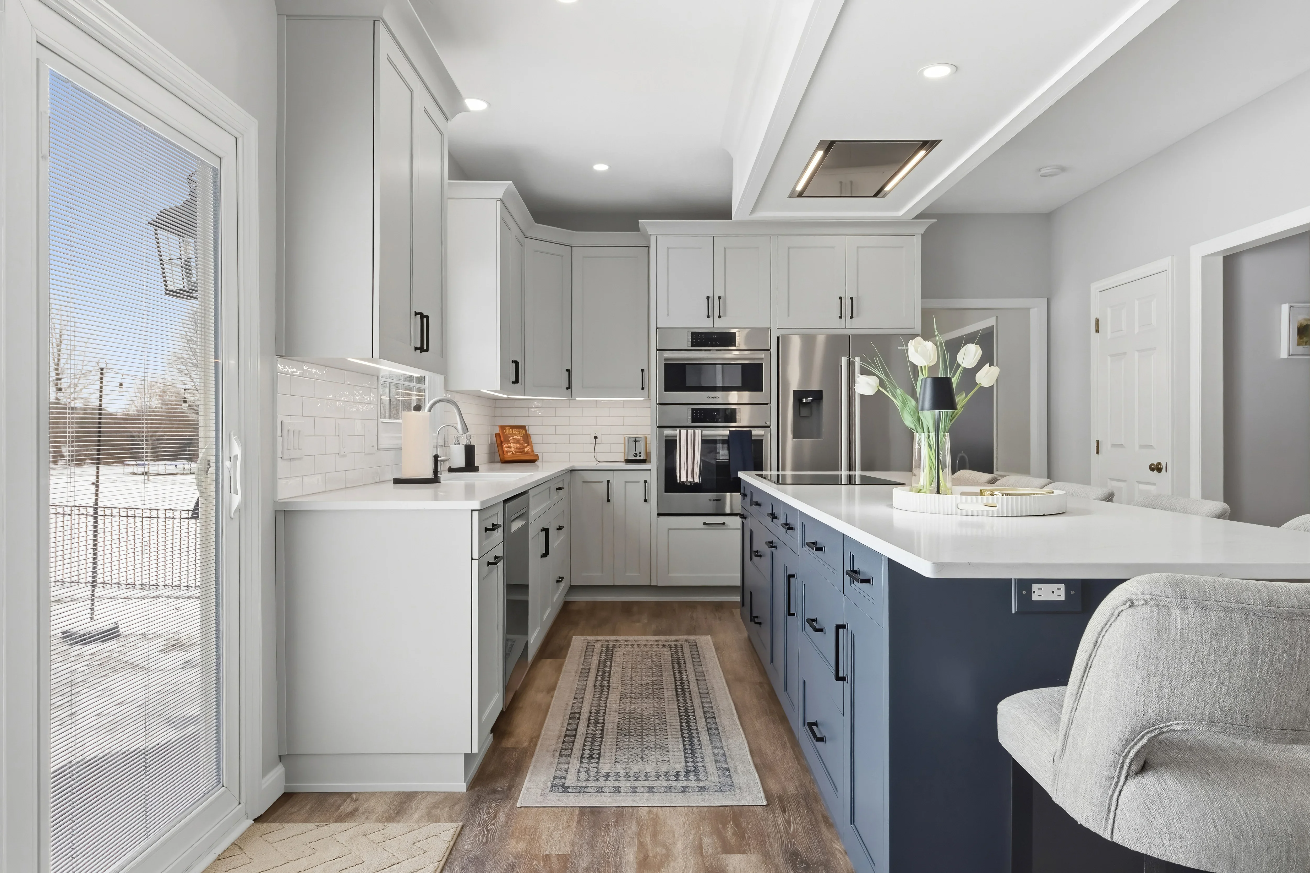 Modern kitchen with white and navy cabinetry, quartz counters, stainless steel appliances, and subway tile backsplash
