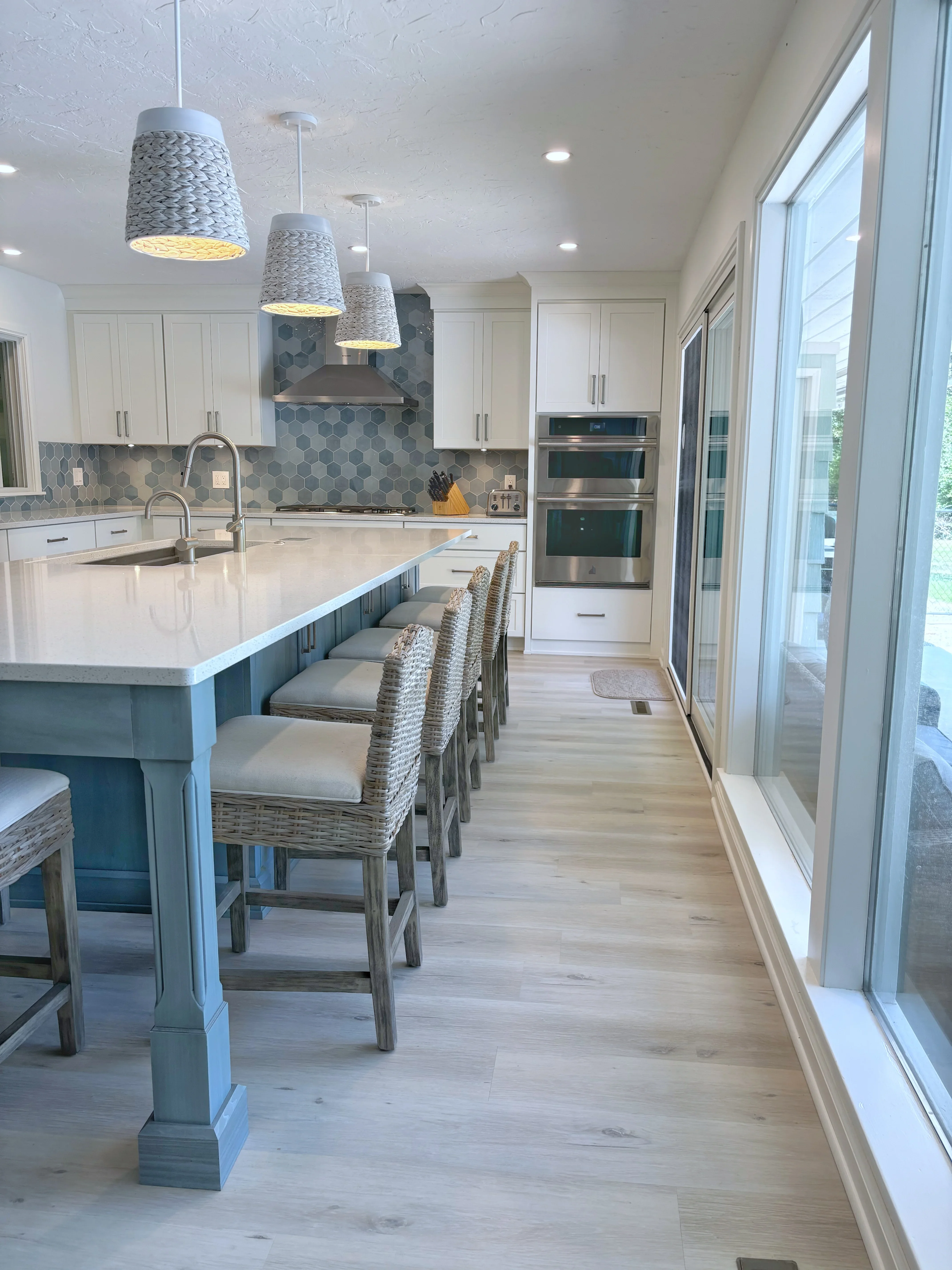 Modern kitchen with white cabinetry, teal island, quartz counters, hexagonal backsplash, and pendant lighting