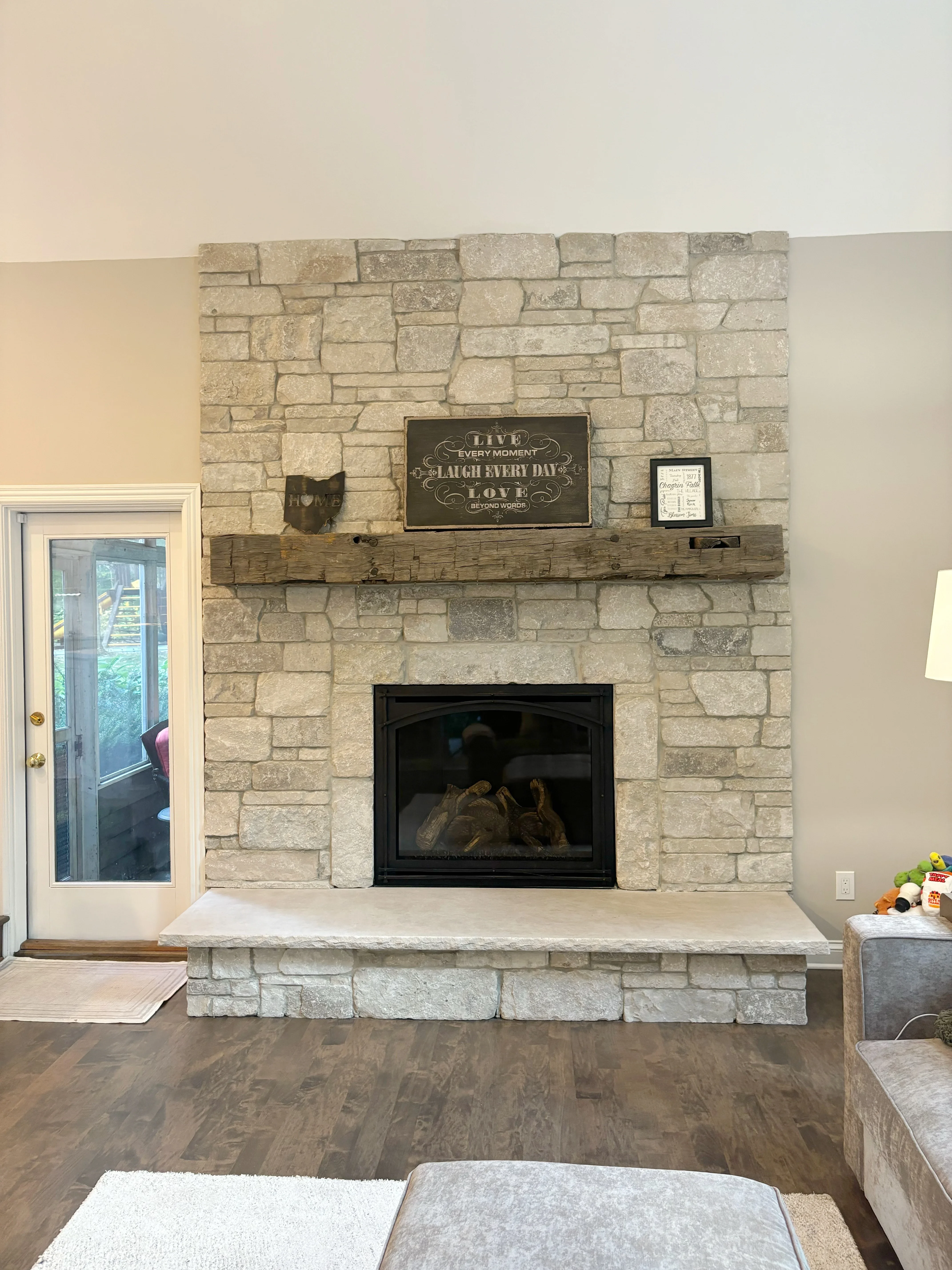 Stacked stone fireplace with black insert, timber mantel, and light stone hearth