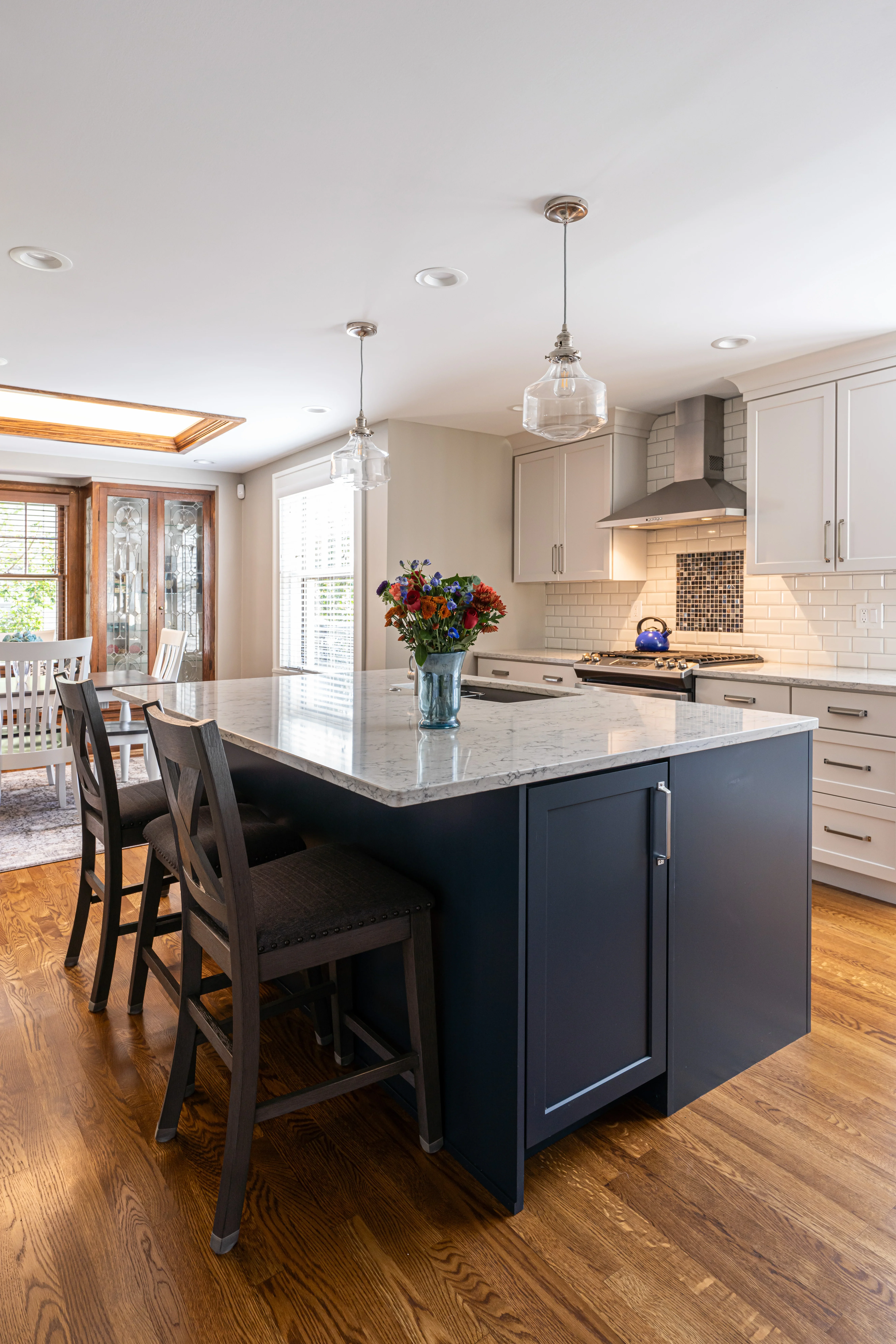 Modern kitchen with navy island, marble countertops, white cabinetry, and glass pendant lights