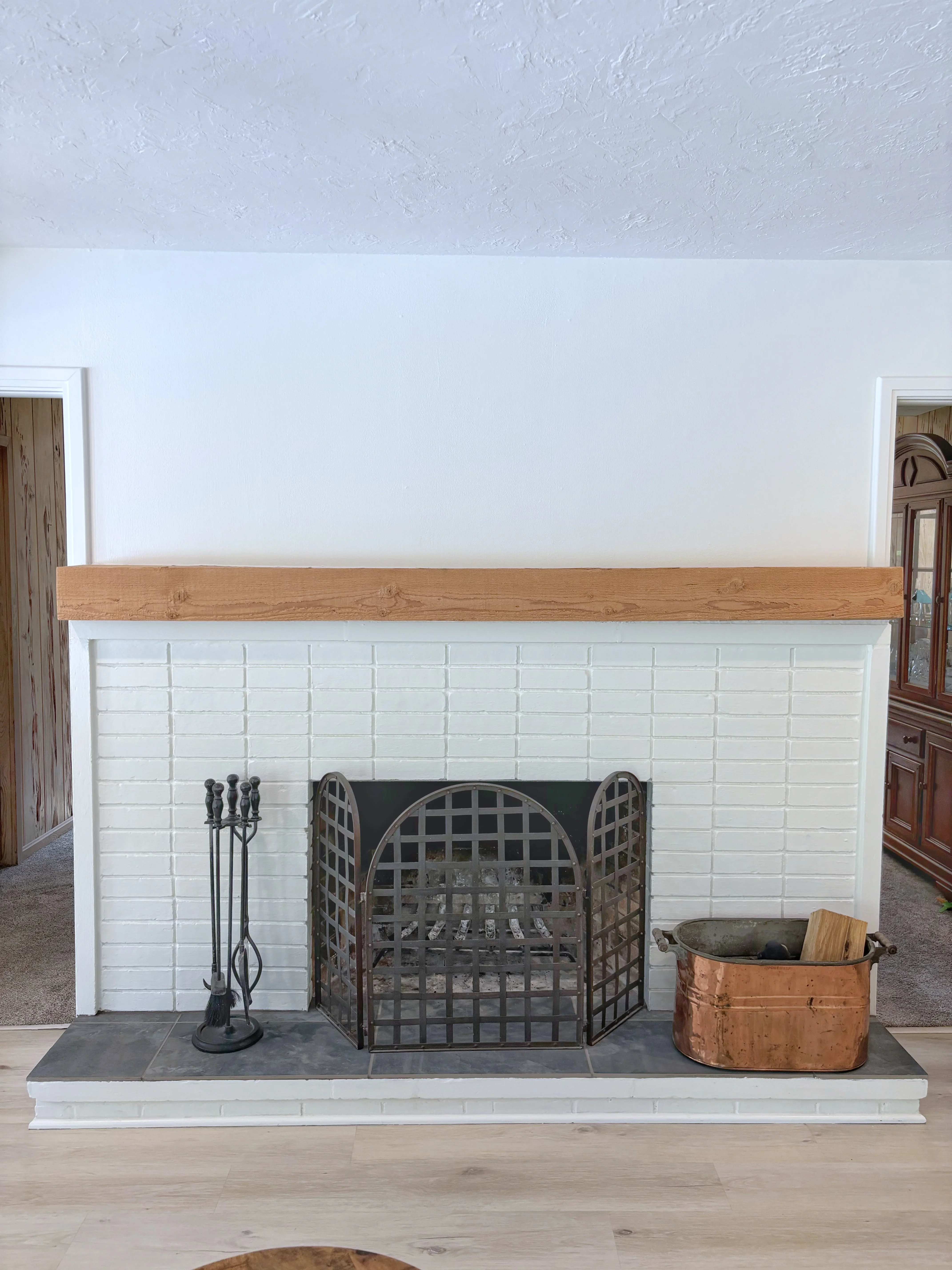 White subway tile fireplace surround with wood mantel, slate hearth, and black iron fireplace tools