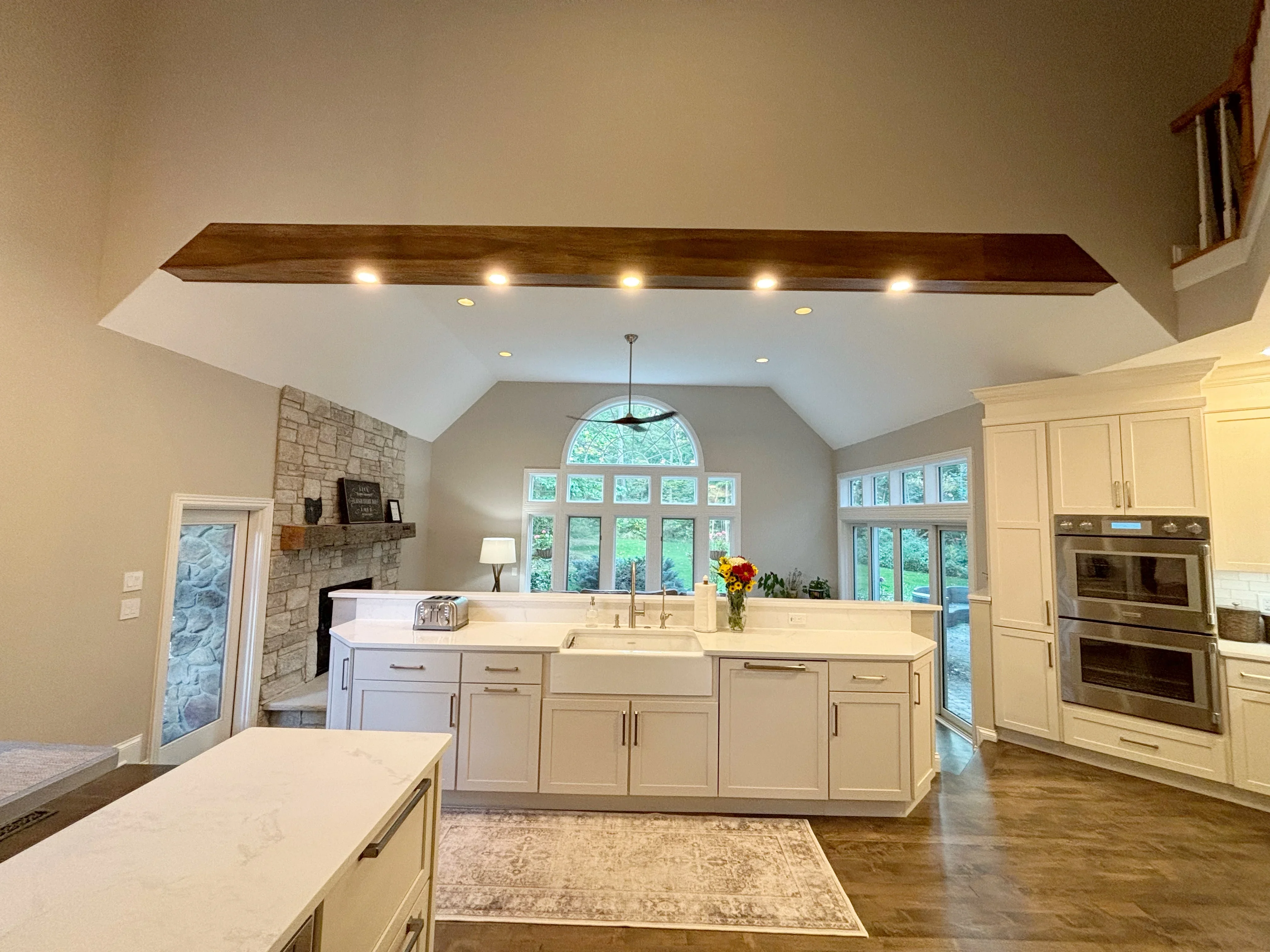 White kitchen with island, quartz counters, coffered ceiling with wood beam, dual ovens, and stone fireplace