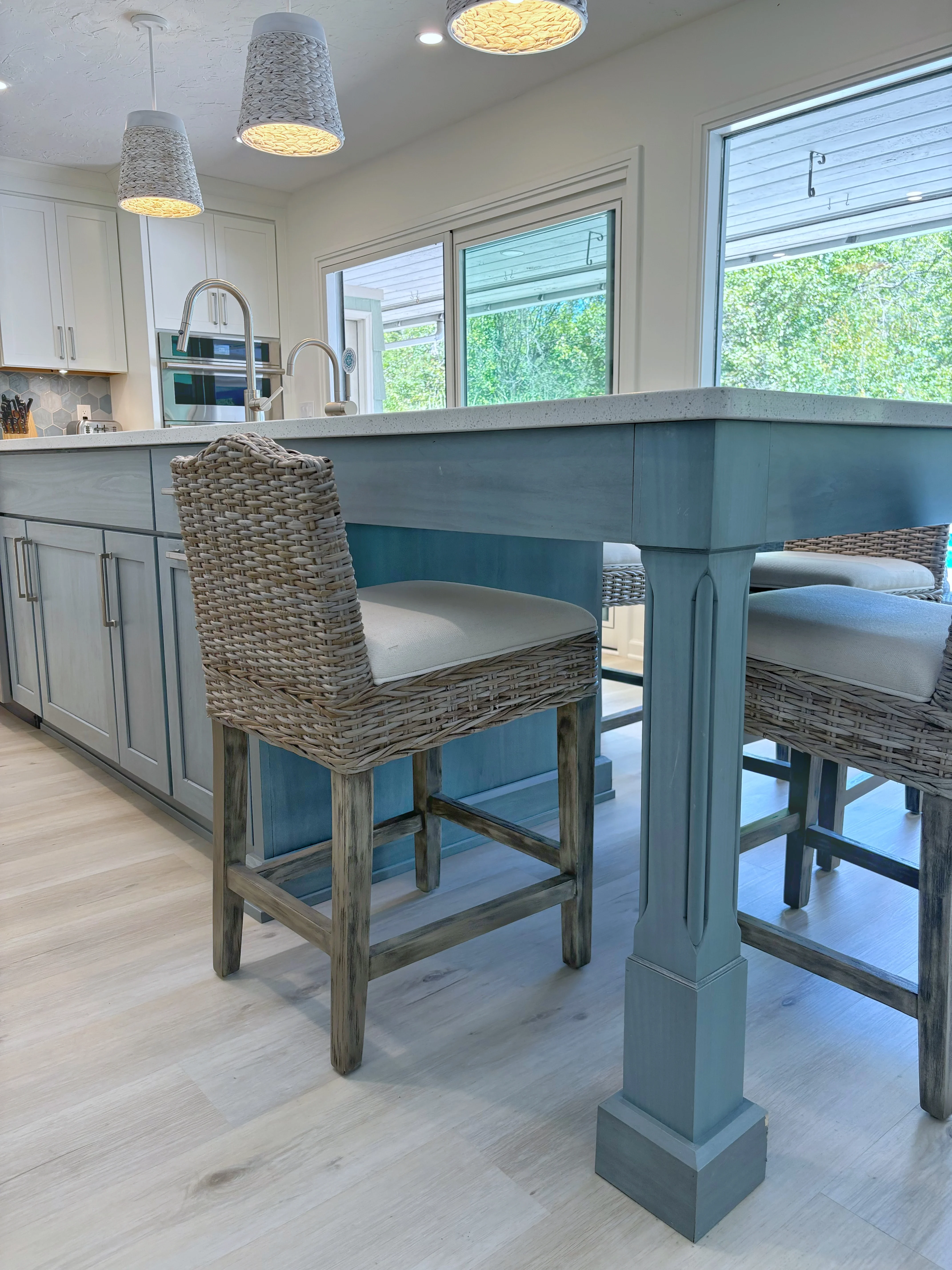 Modern kitchen with teal island, concrete waterfall countertop, white cabinetry, and rattan bar seating