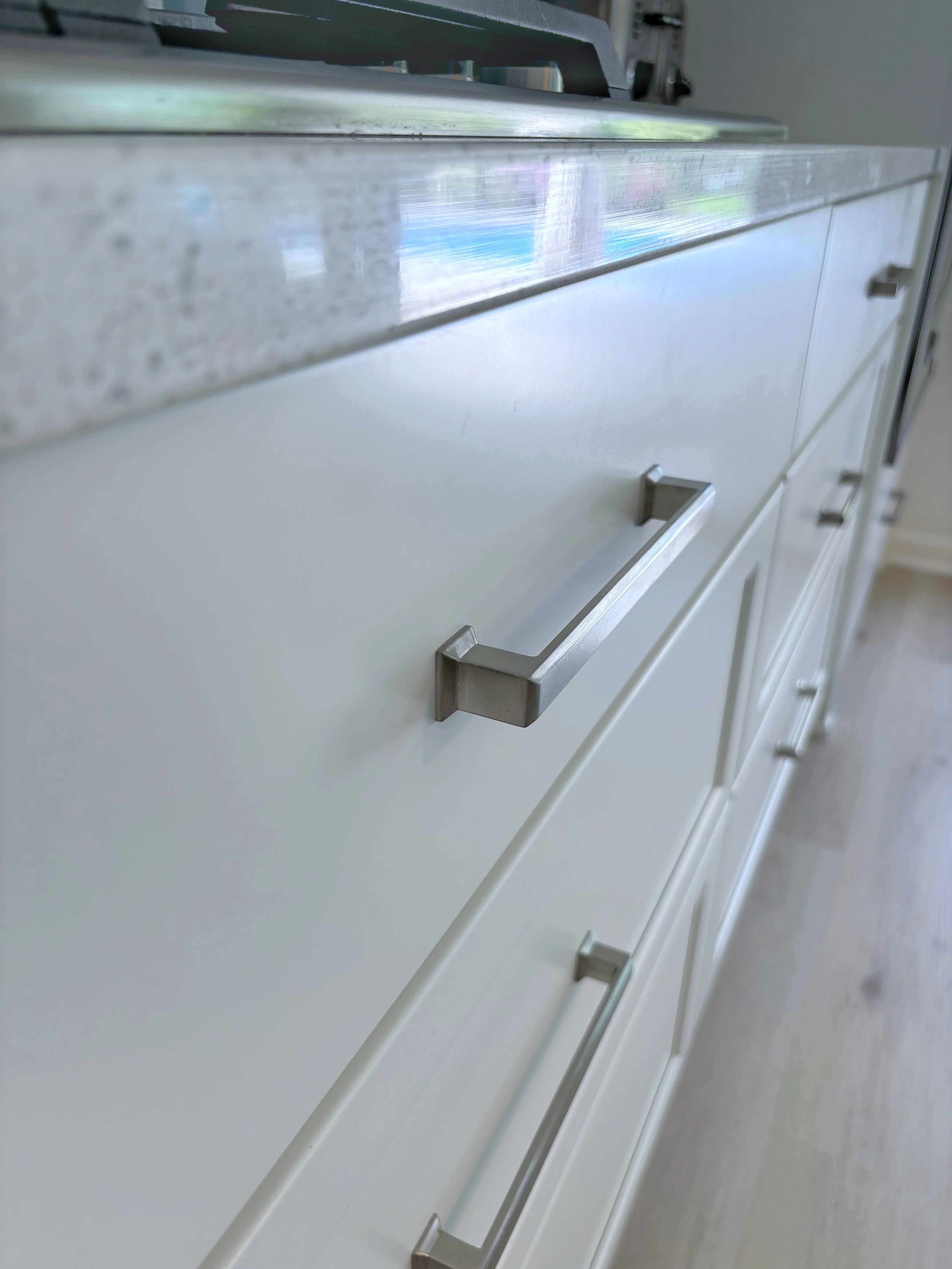 White kitchen cabinets with brushed nickel handles and marble backsplash with metal trim