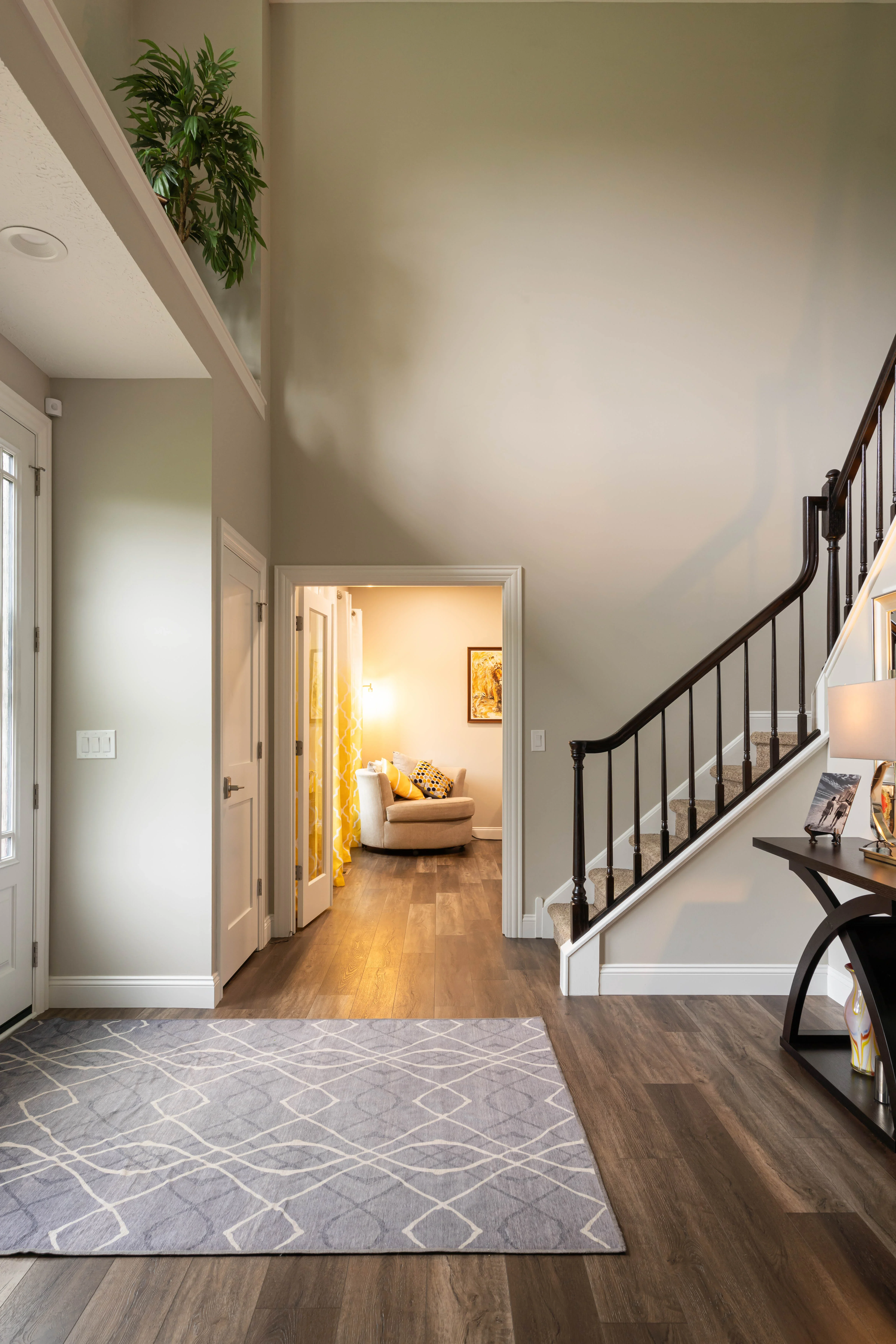 Entryway with black iron staircase railing, hardwood floors, geometric area rug, and neutral walls