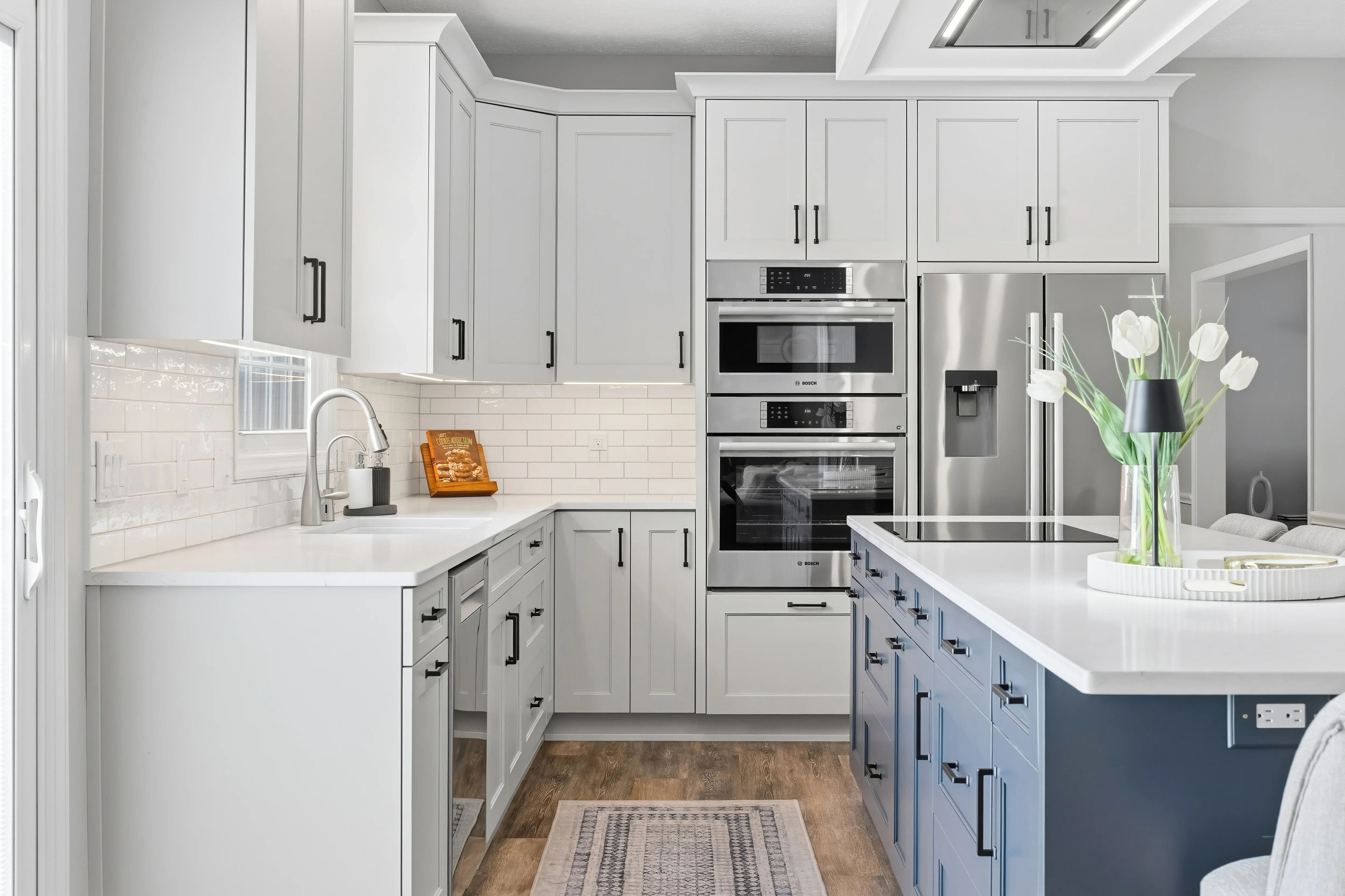 Modern kitchen with white and navy cabinetry, white quartz counters, subway tile backsplash, and stainless steel appliances