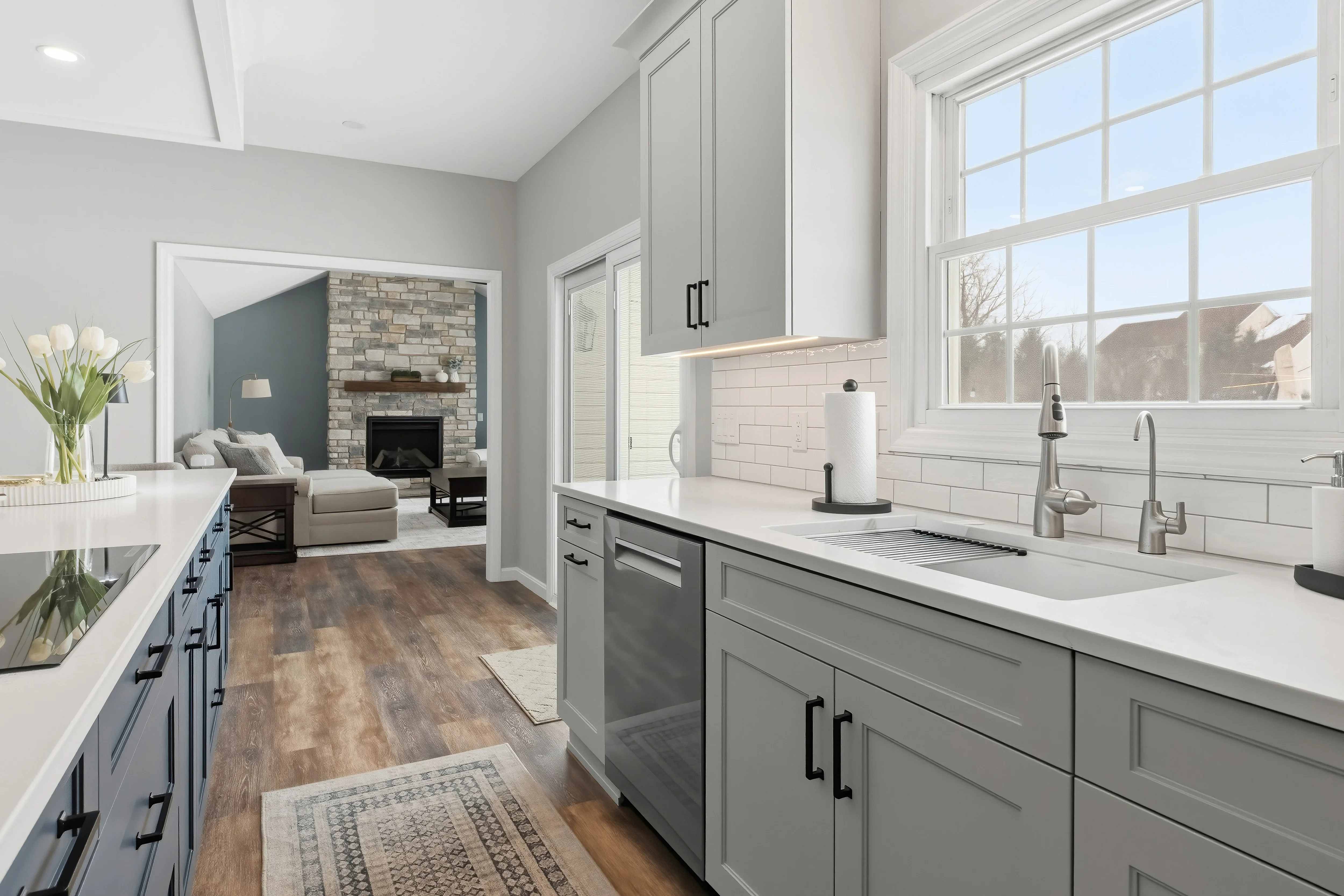 Modern kitchen with gray cabinetry, white subway tile, quartz counters, and open view to living room with fireplace