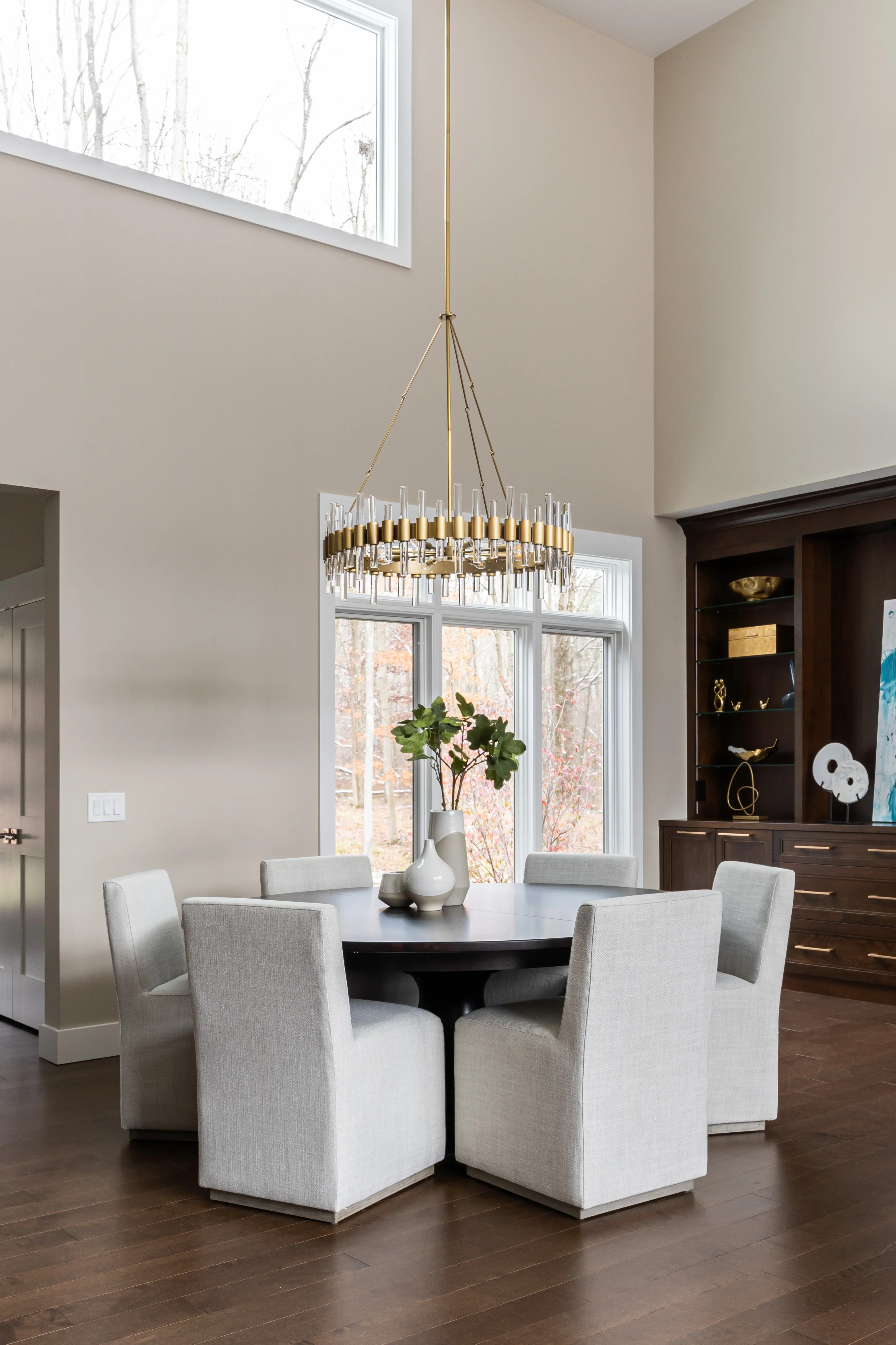 Modern dining room with brass pendant, round black table, upholstered chairs, and custom dark wood cabinetry